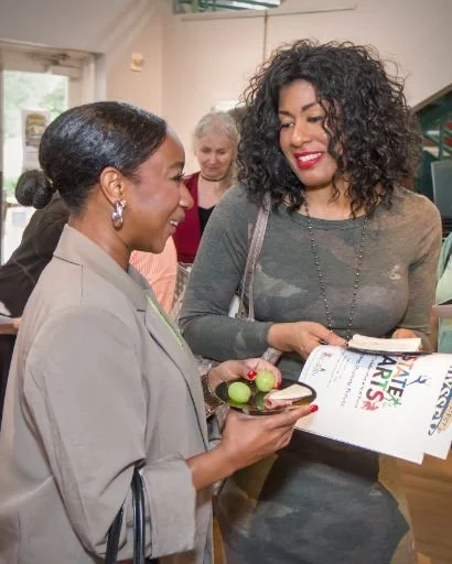 Two women smiling and talking at an art exhibit, with a woman in the background.