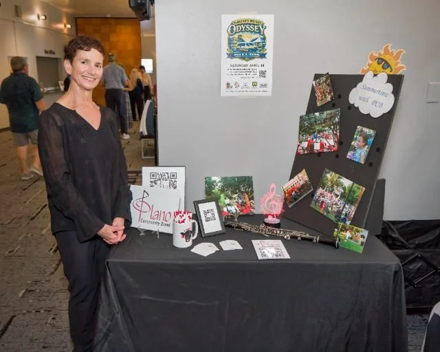 A woman stands smiling next to a table display with photos, QR codes, and decorations at an indoor event.
