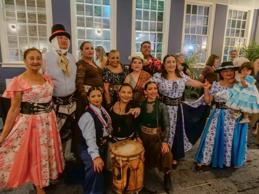 Group of people dressed in traditional Mexican attire, celebrating at an indoor event.