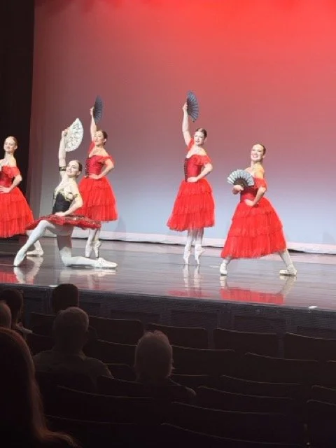 Five ballet dancers on stage, wearing red and black costumes with fans, performing in front of an audience.