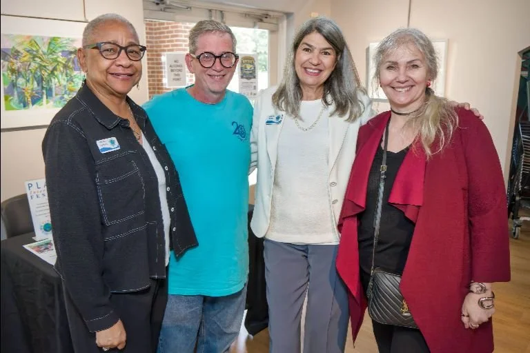 Four adults standing together indoors, smiling at the camera.