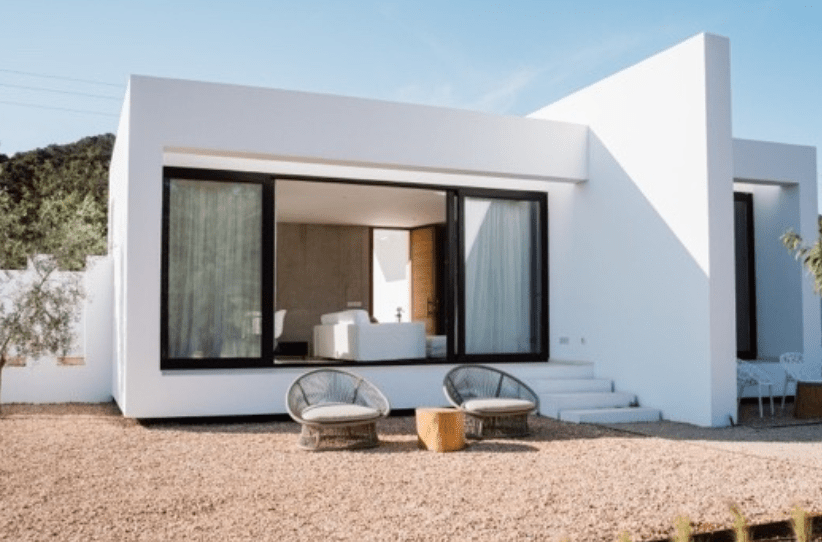 Modern white house with large glass sliding doors, outdoor seating, and a gravel yard with steps leading to the entrance.