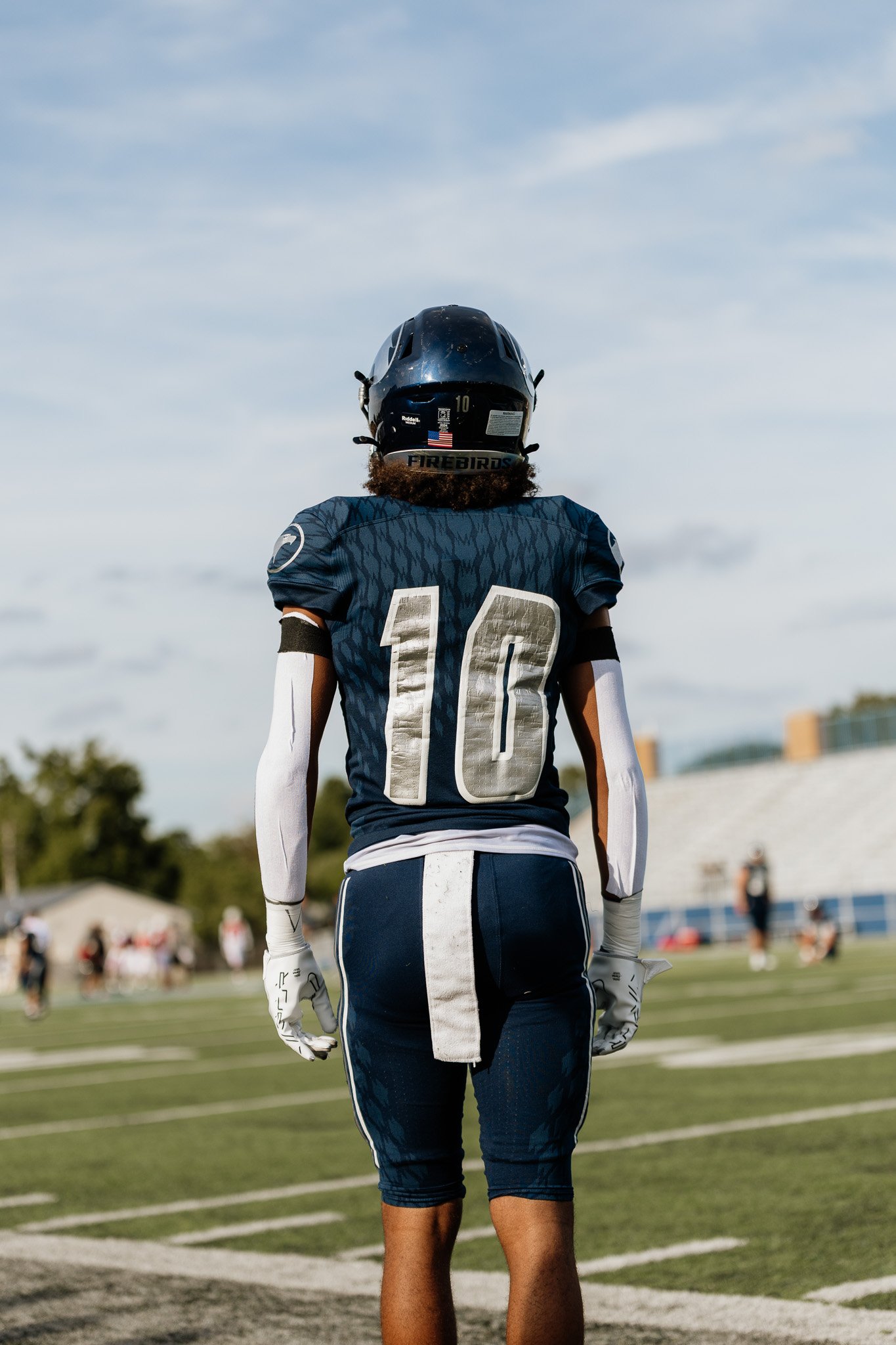 A football player in jersey number 10 standing on the field, facing away, wearing a helmet and gloves.