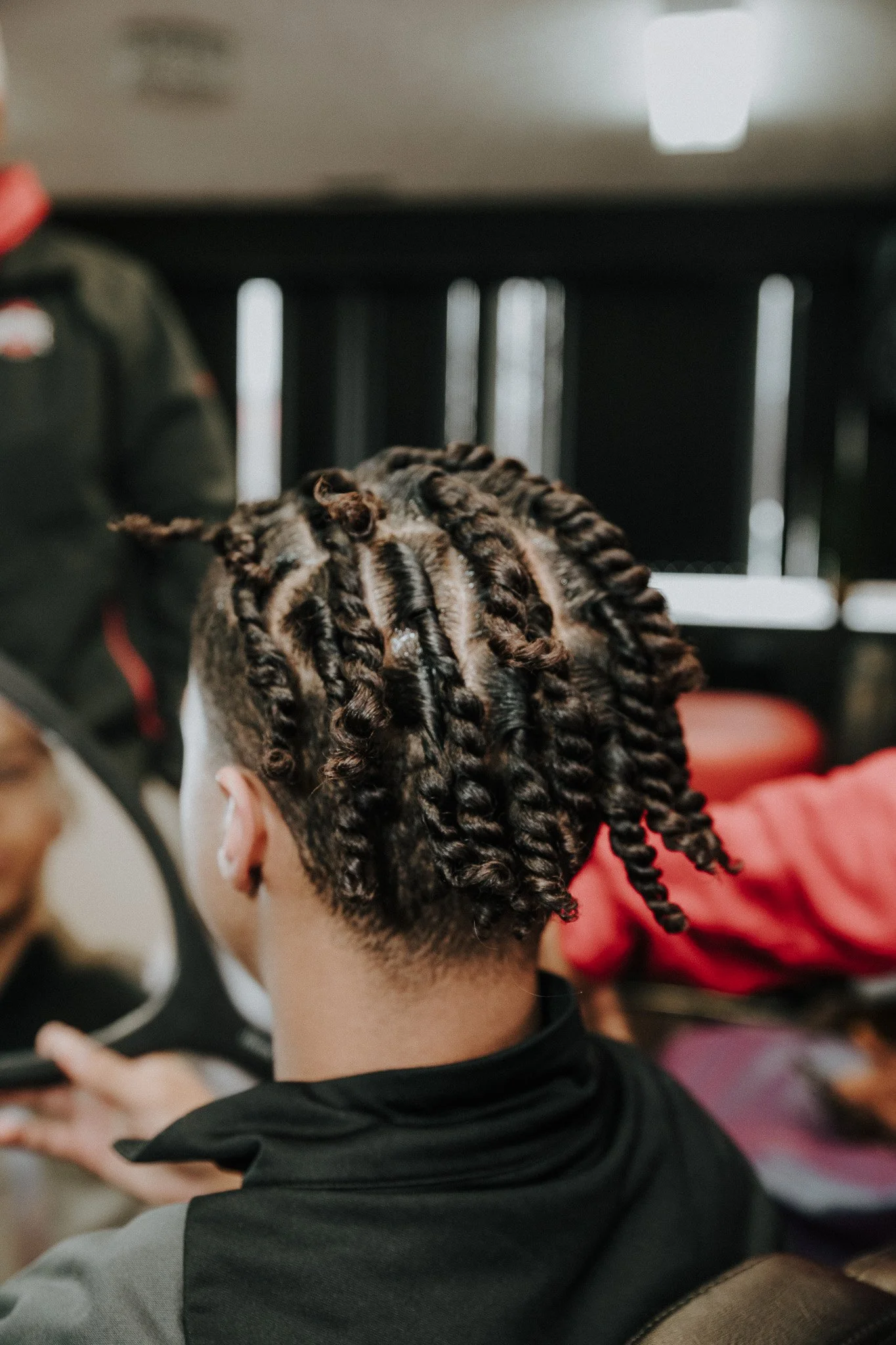 Person with short curly hair in twisted braids, sitting indoors.