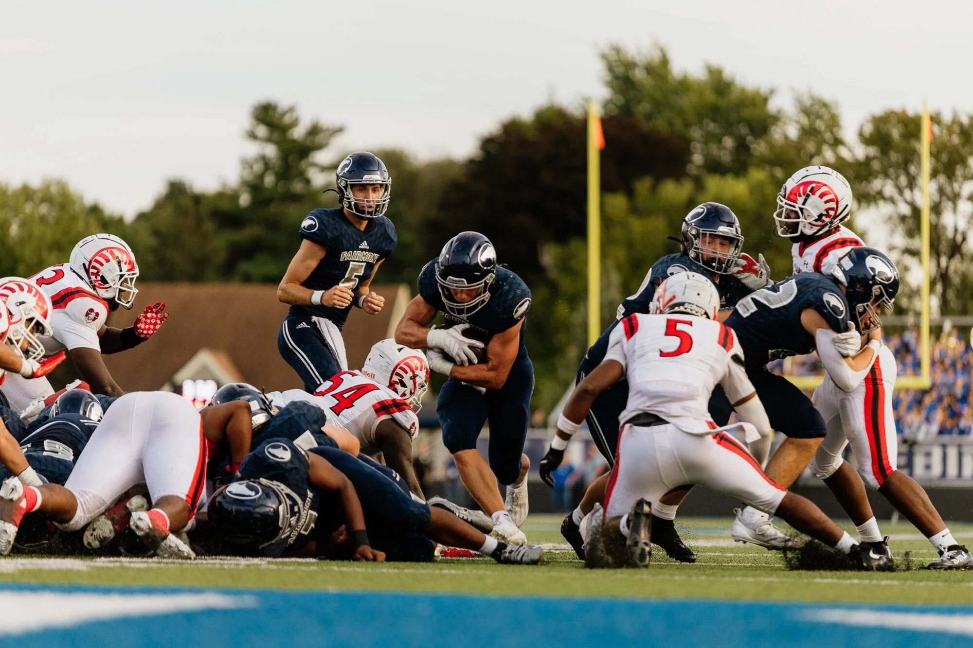 American football game with players tackling and blocking on the field during sunset.