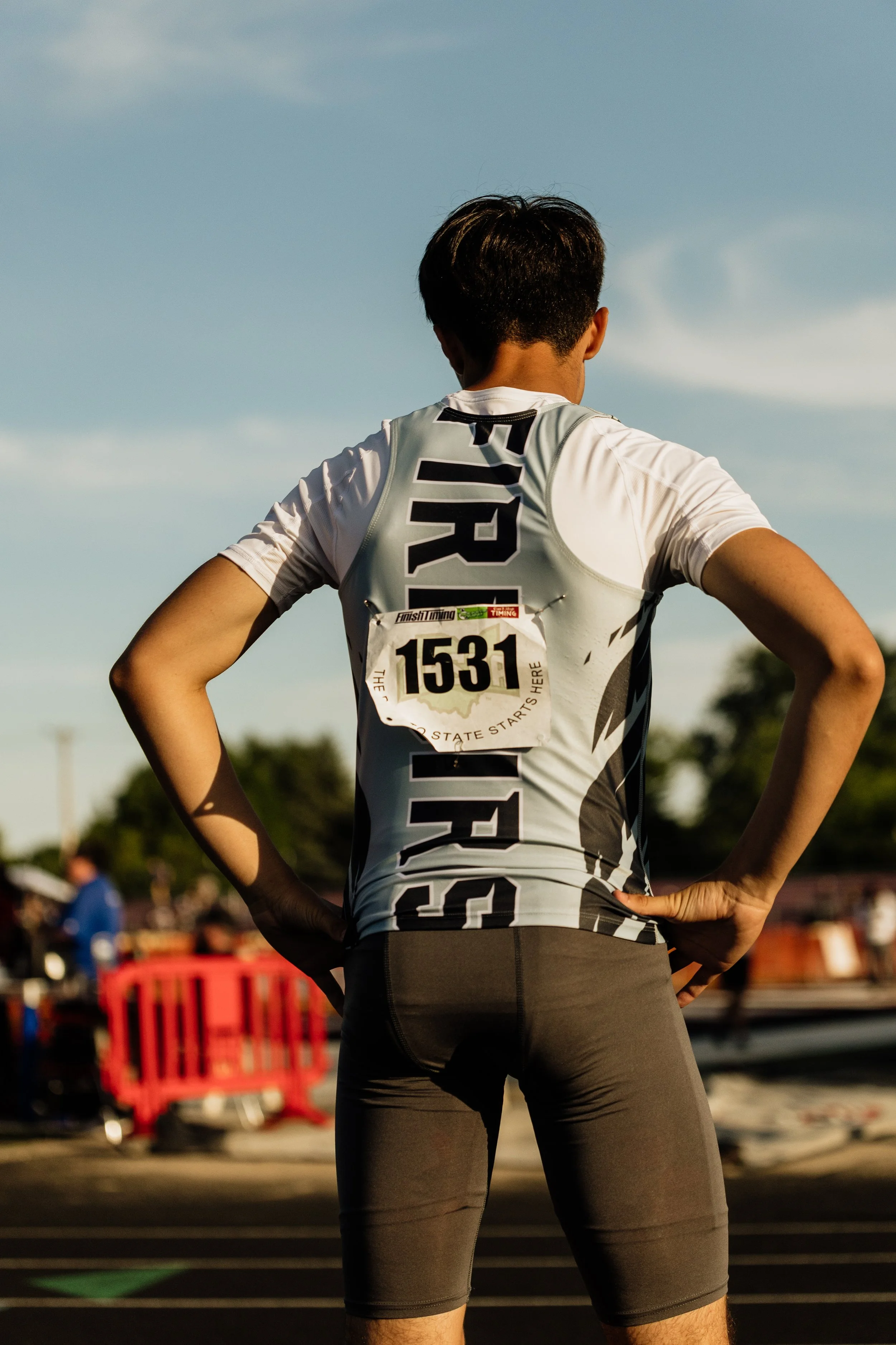 A male athlete stands with hands on hips, wearing a race bib number 1531, at a running track during sunset.