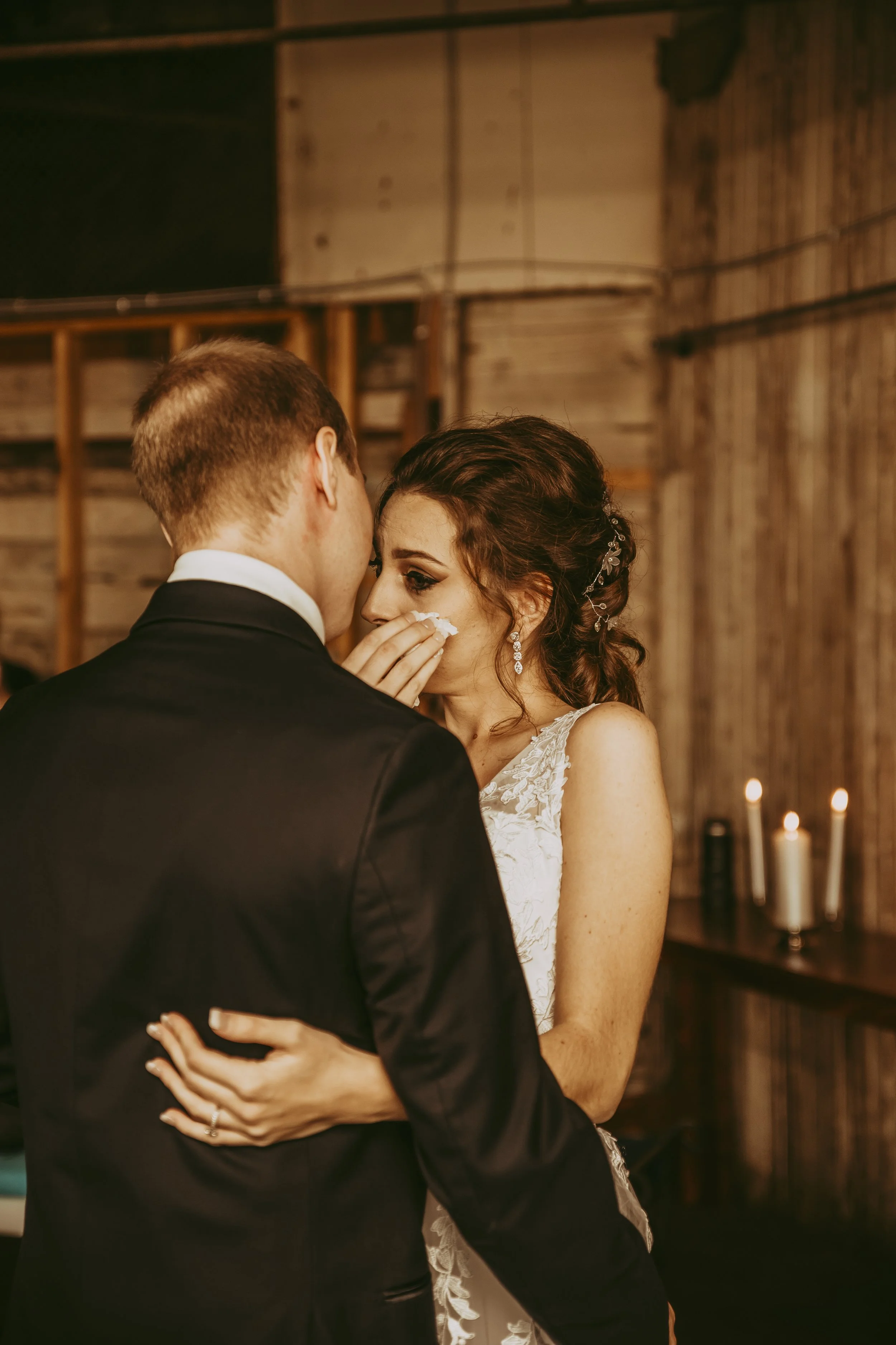 A bride and groom share an emotional moment during their wedding dance, with the bride wiping a tear from her eye.