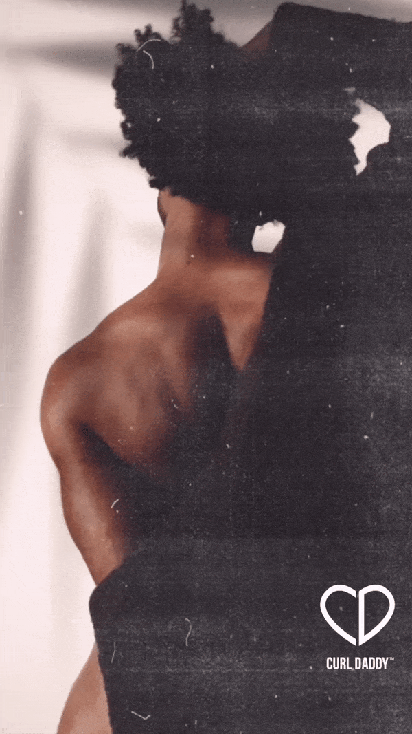 Close-up of a person with dark skin and natural curly hair, partly covered with black clothing, showing their shoulder and back.