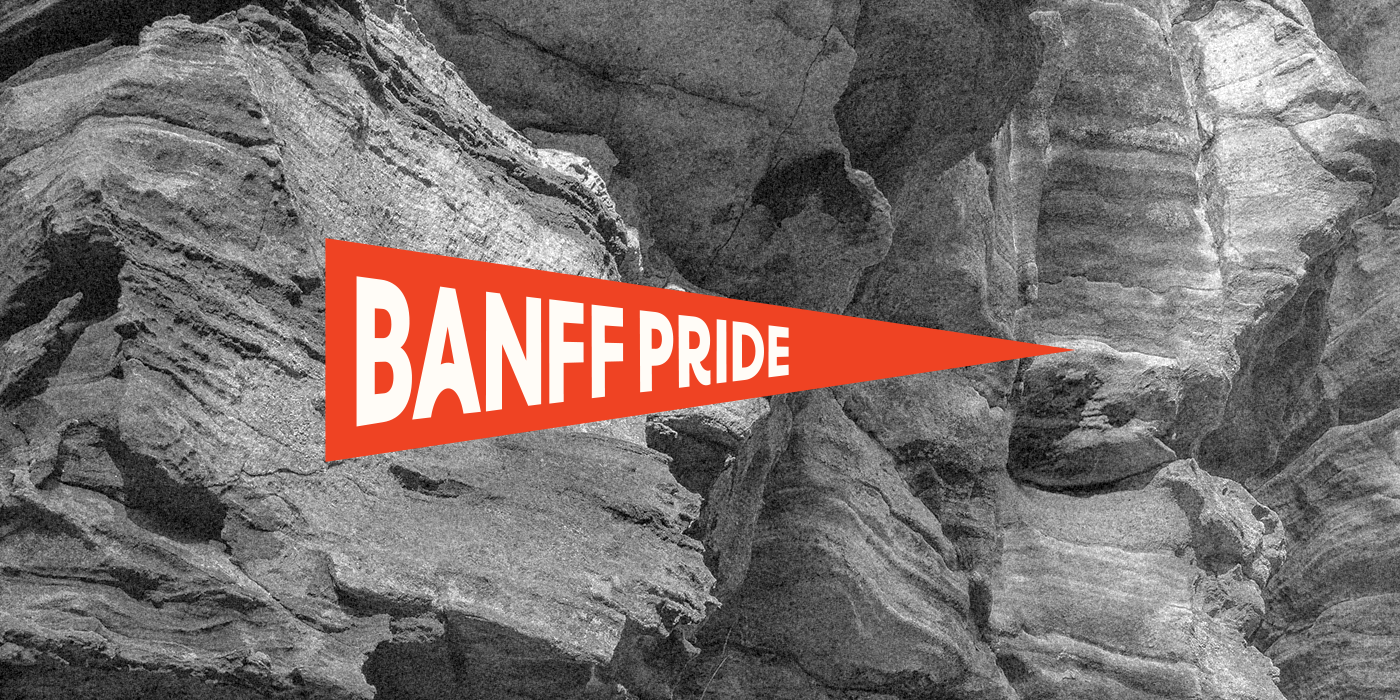 Black and white photo of rocks with red triangular flag that reads "BANFF PRIDE" in white bold letters.