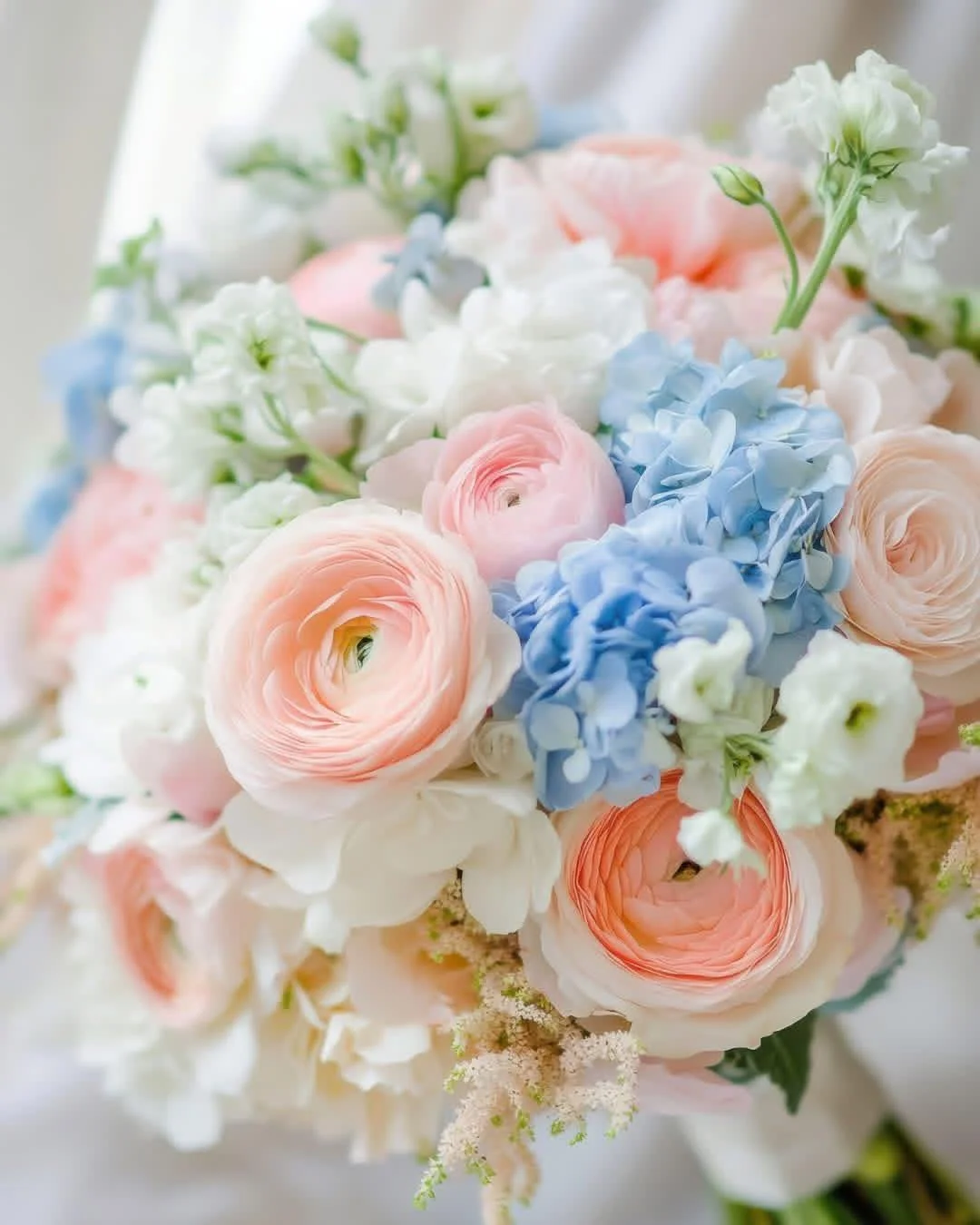 💕 Delicate blush ranunculus float among powder blue hydrangeas and crisp white blooms. The soft color palette creates a watercolor effect that feels timeless and fresh&mdash;the perfect choice for spring weddings or brides seeking subtle sophisticat