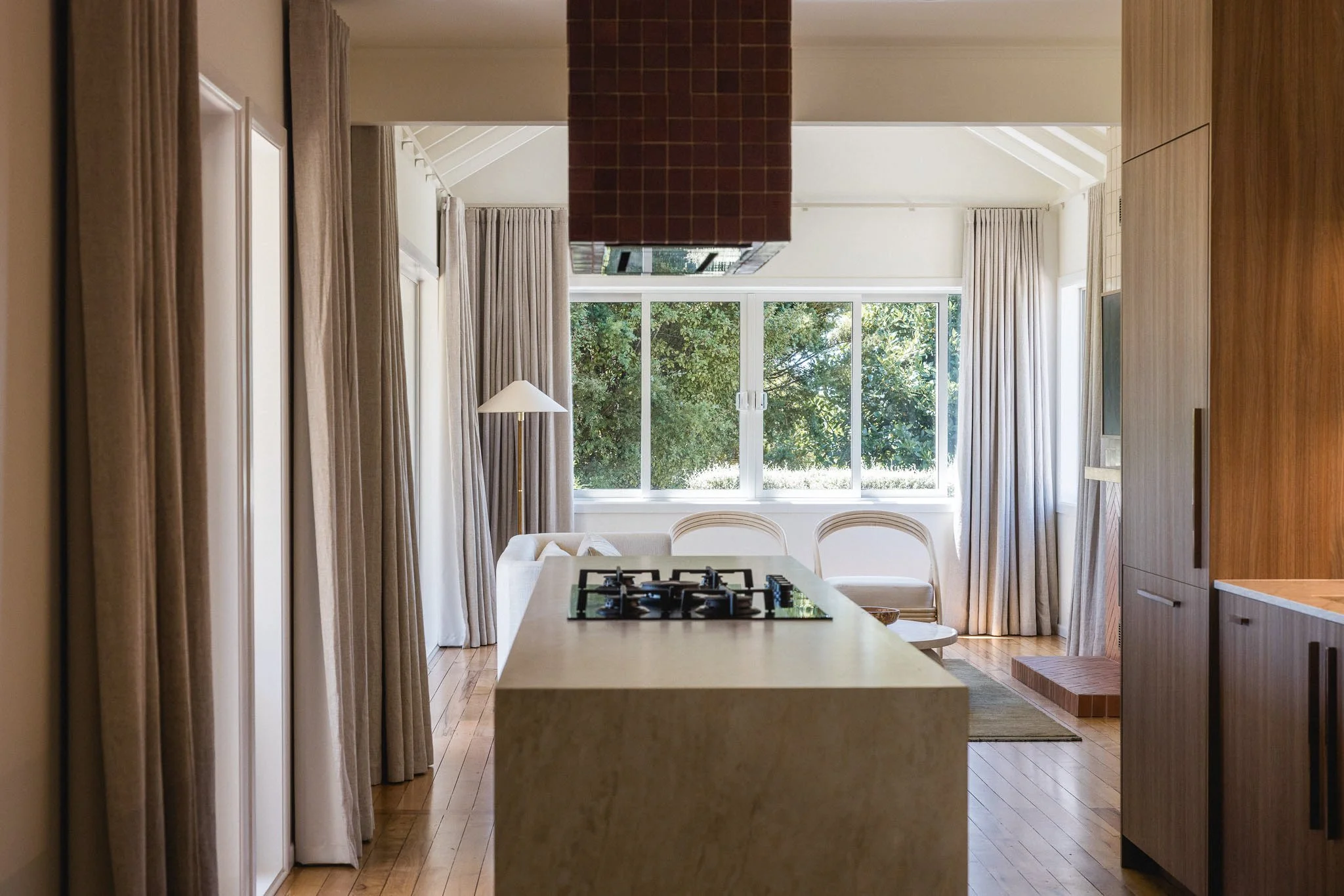 Modern kitchen with marble island, gas cooktop, large window, and neutral curtains