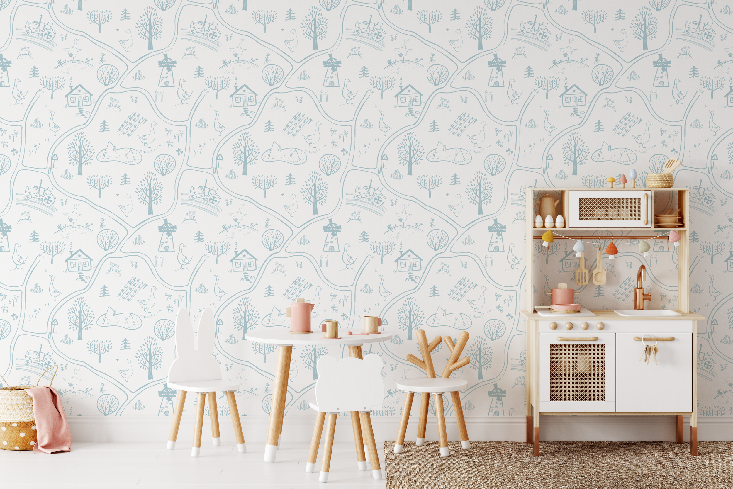 Children's play kitchen with white and wood accents, set against blue and white wallpaper with farming and countryside illustrations, next to a small table with pink and beige toys and two chairs with bunny and apple shapes, on a white floor with a woven basket and pink cloth nearby.