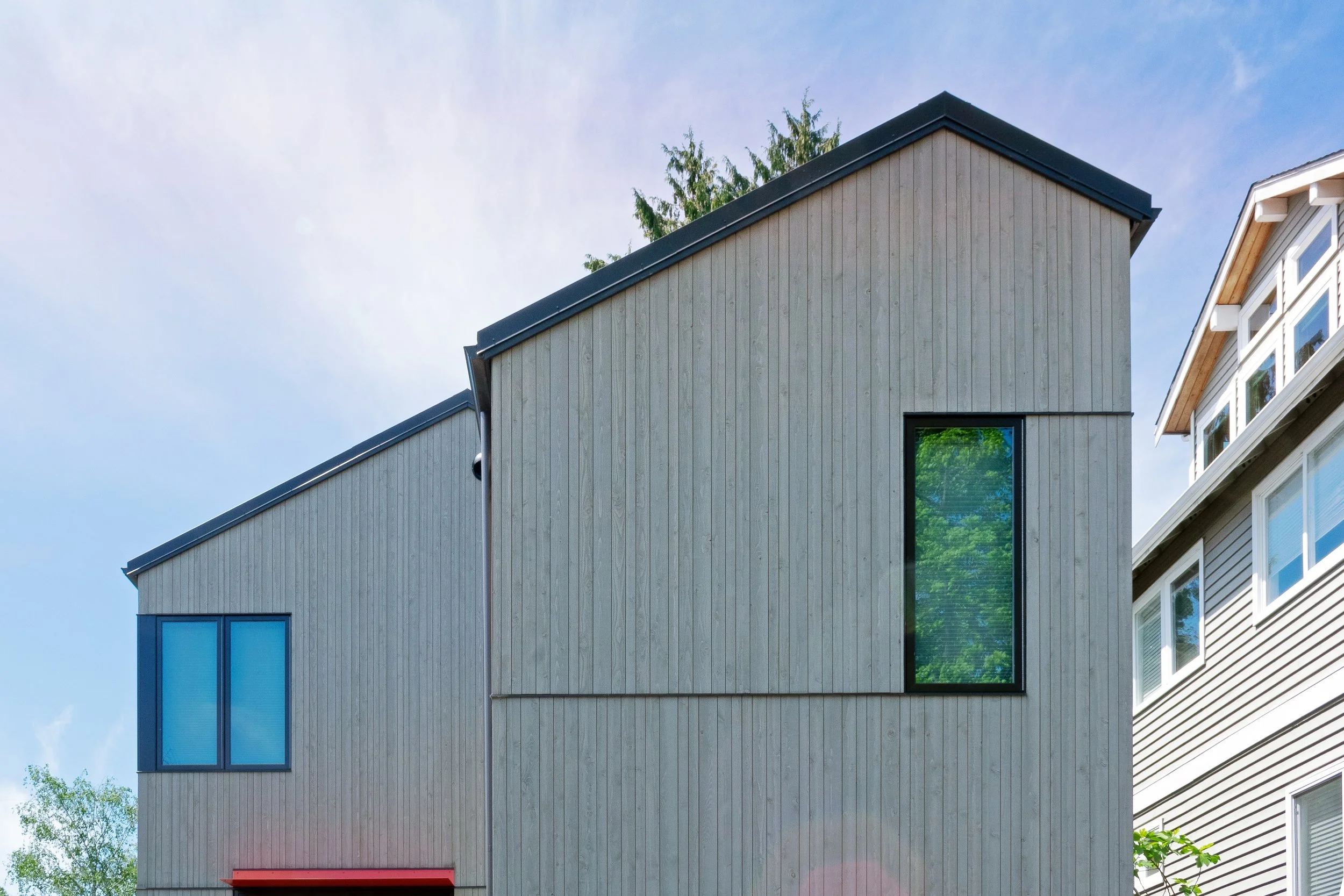 Modern wooden house exterior with large windows under a clear blue sky.