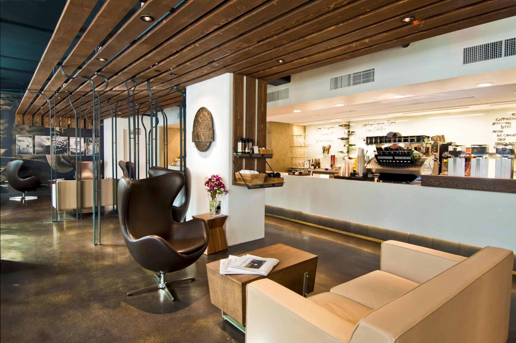 Modern coffee shop interior with wooden accents, leather chairs, and a coffee counter with an espresso machine.