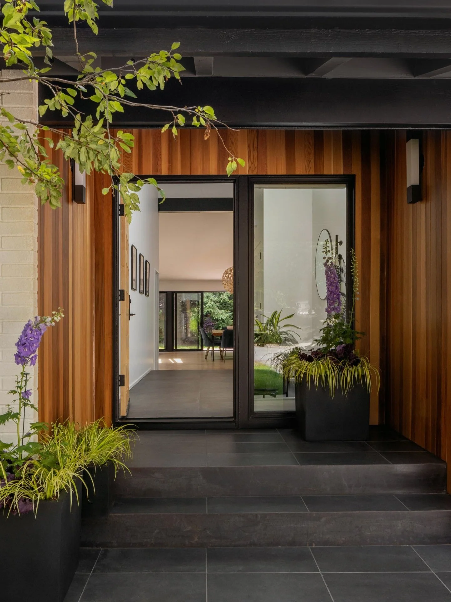 Modern house entrance with wooden siding, glass door, and potted plants.