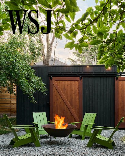 Four green Adirondack chairs arranged around a steel fire pit with flames with a custom wood shed in the background. Featured in the Wall Street Jounal.
