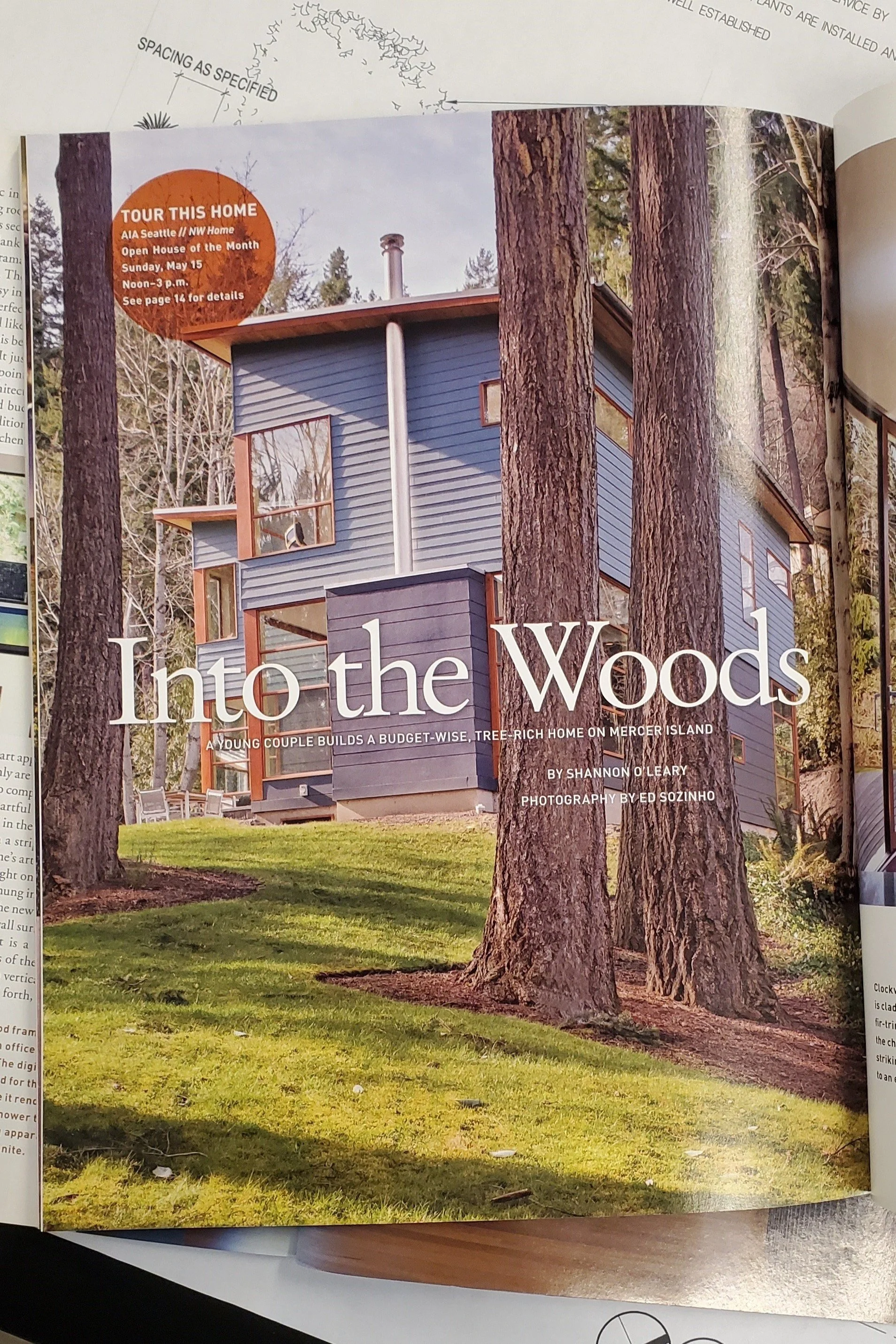 Modern house with large windows surrounded by trees, featured in a magazine with the headline 'Into the Woods' about a budget-wise home on Mercer Island.