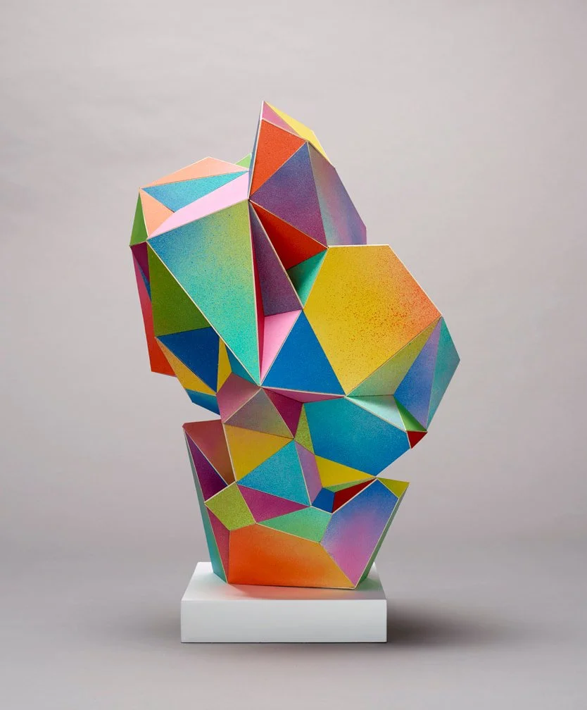 Colorful geometric sculpture with various triangles and polygons on a white base against a gray background.