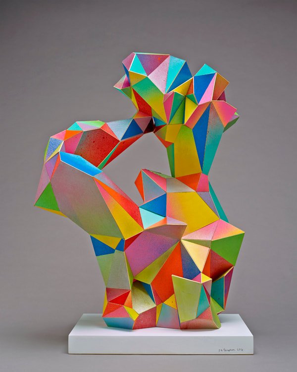 Colorful geometric sculpture resembling a faceted figure, placed on a white pedestal against a gray background.