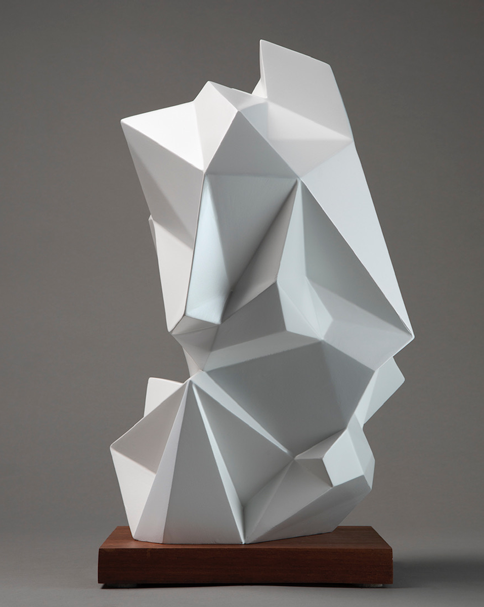 Abstract geometric white sculpture with sharp angular facets mounted on a wooden base.