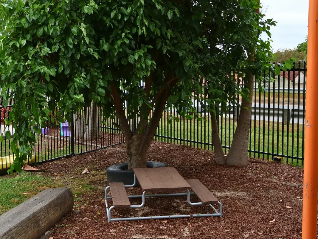 Children's picnic table under a leafy green tree in the natural outdoor play area