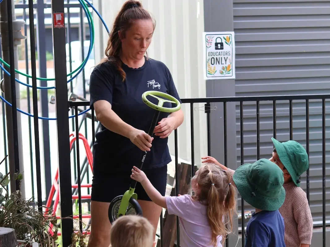 Educator handing out wheely toys to children outdoors