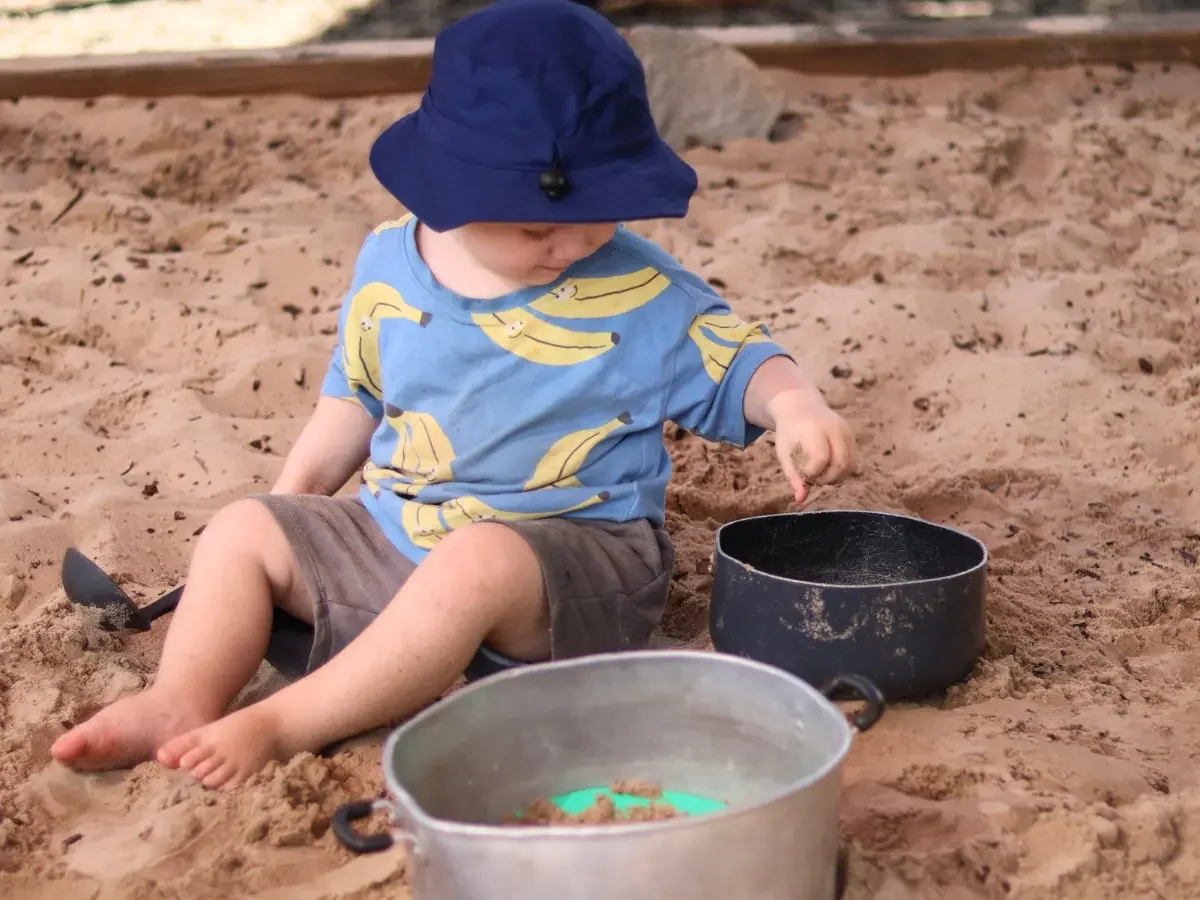 Child playing in the sandpit pouring sand into saucepans