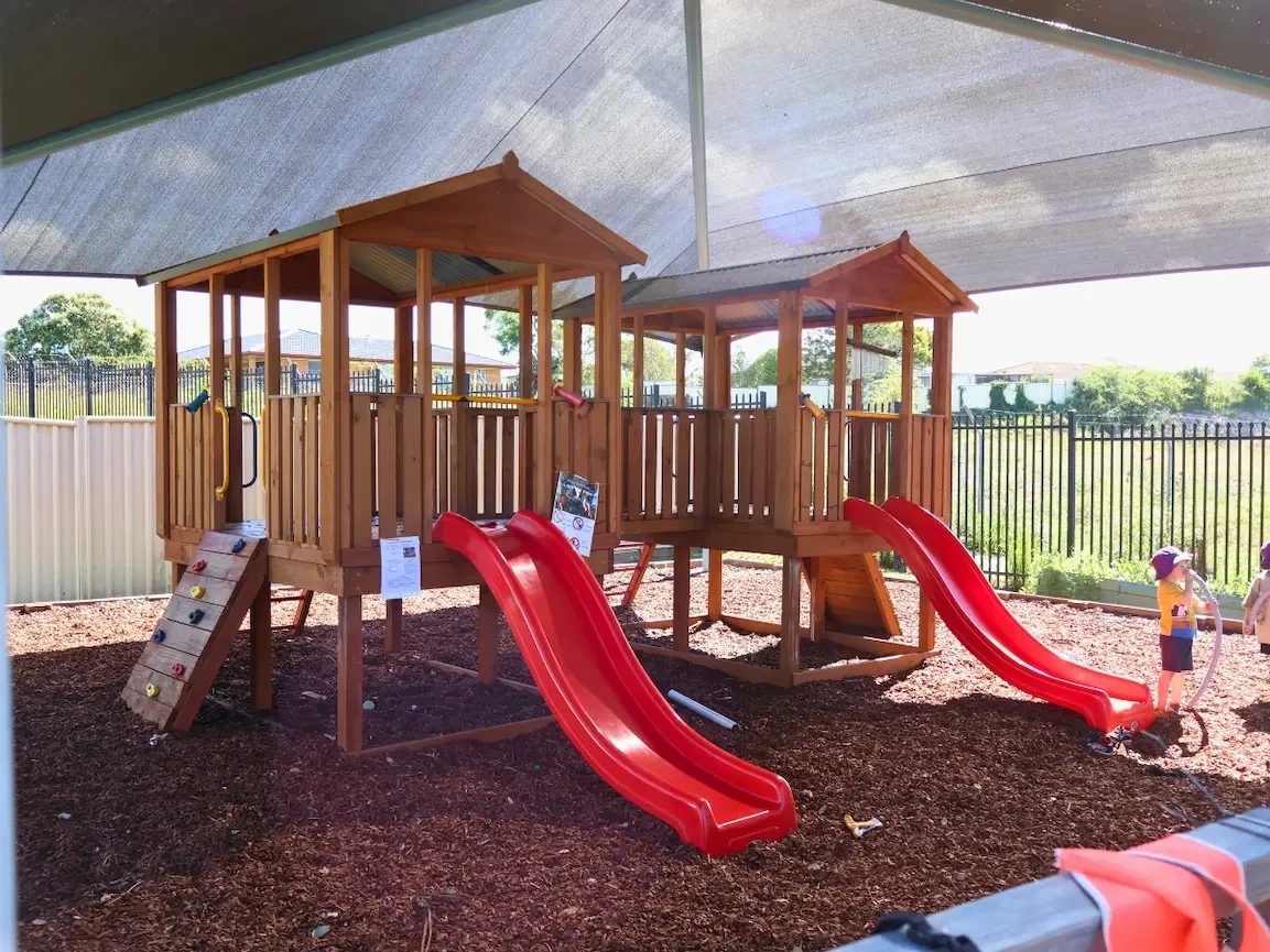 Shaded wooden forts with slides and climbing walls in the outdoor play area