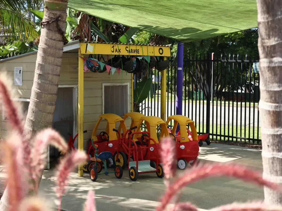 Children's trikes and cozy coupes parked outside a cubby house in the outdoor play area