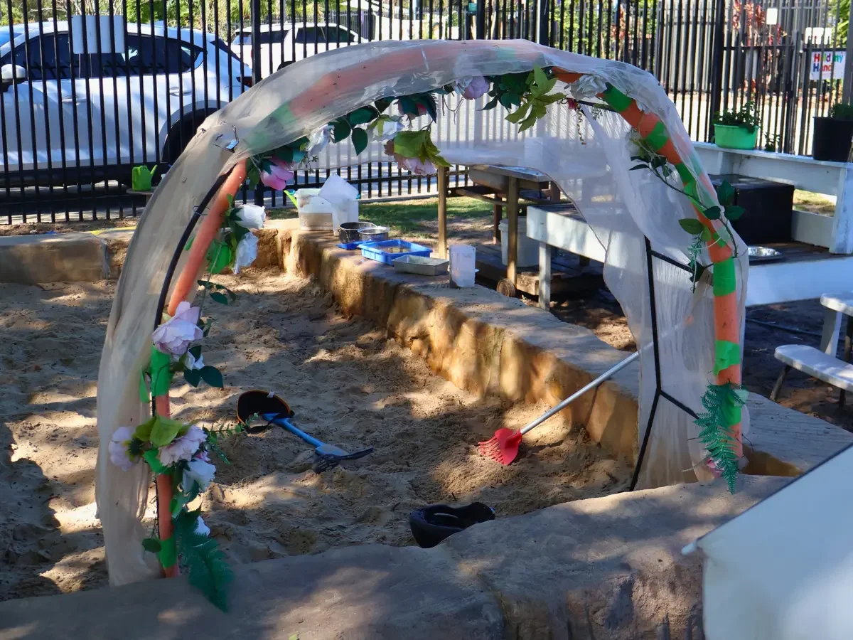 Large sandpit and mud kitchen decorated with a big archway of flowing fabric and flowers