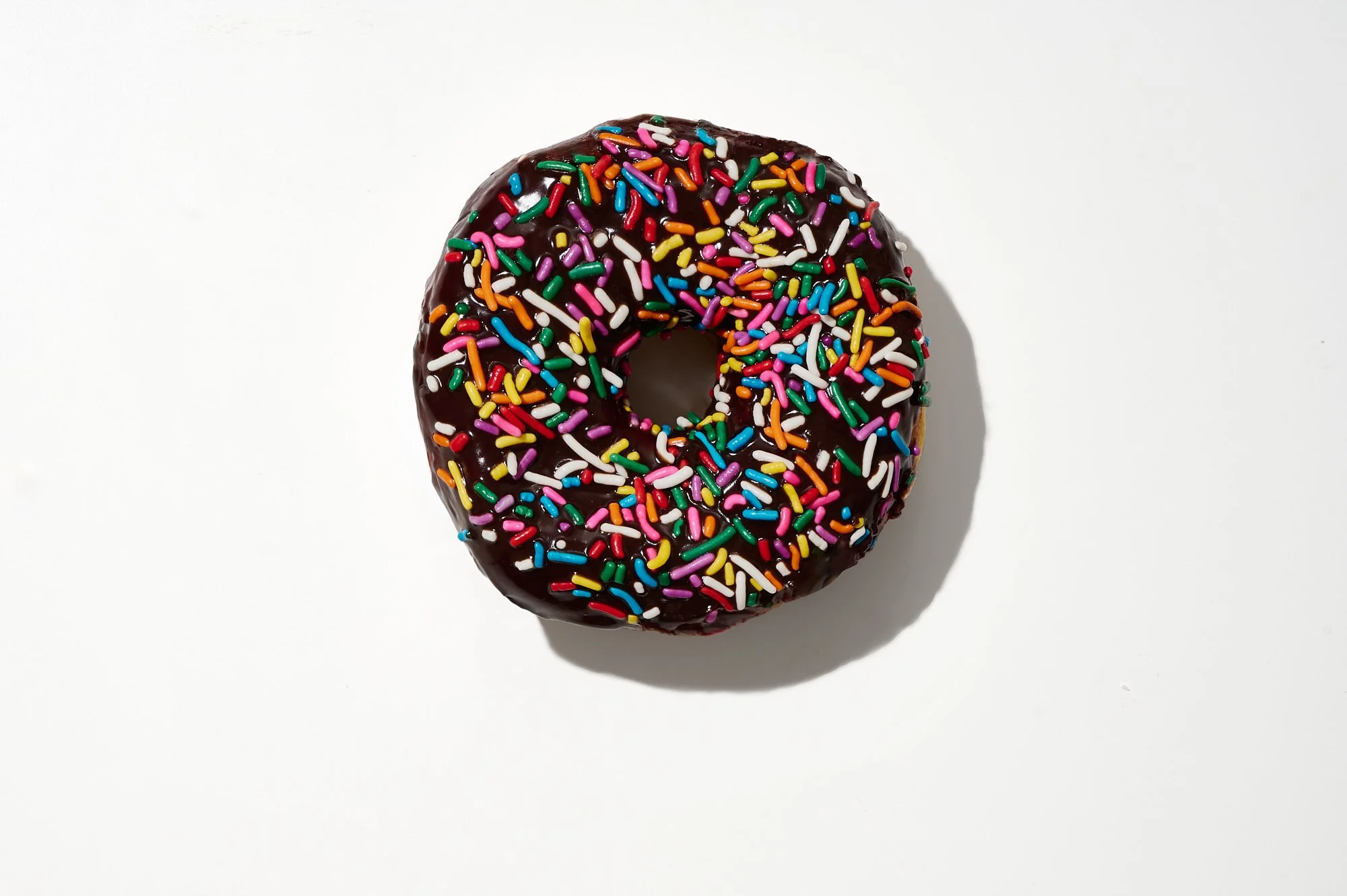 Chocolate-glazed donut with multicolored sprinkles on a white background.