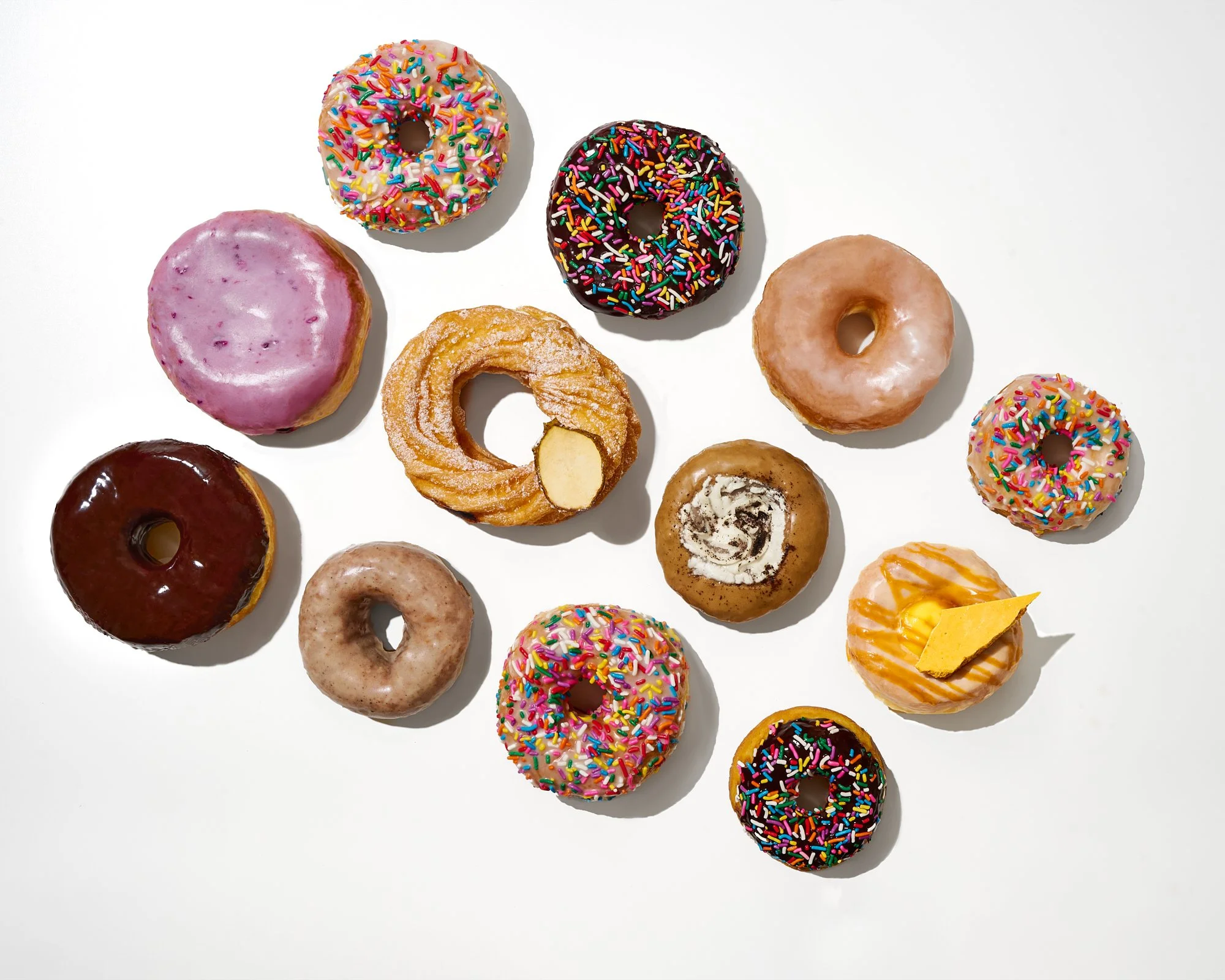 An assortment of colorful donuts with various glazes, sprinkles, and toppings arranged on a white surface.