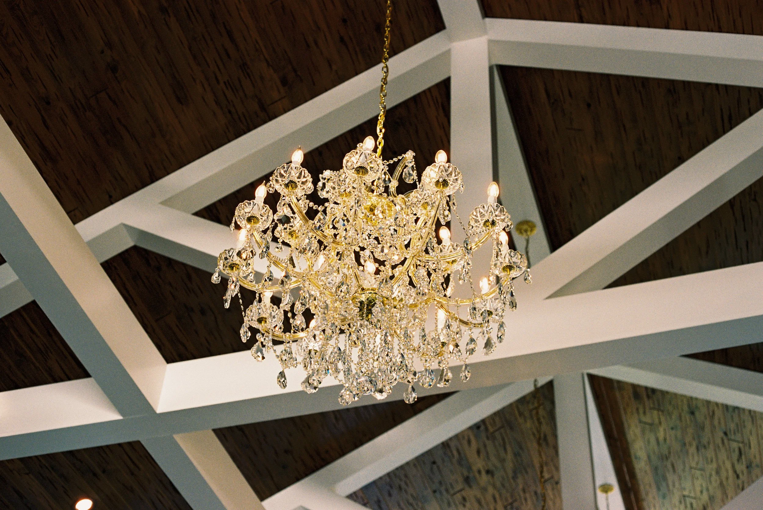 A chandelier hanging from a high wooden ceiling with white beams.