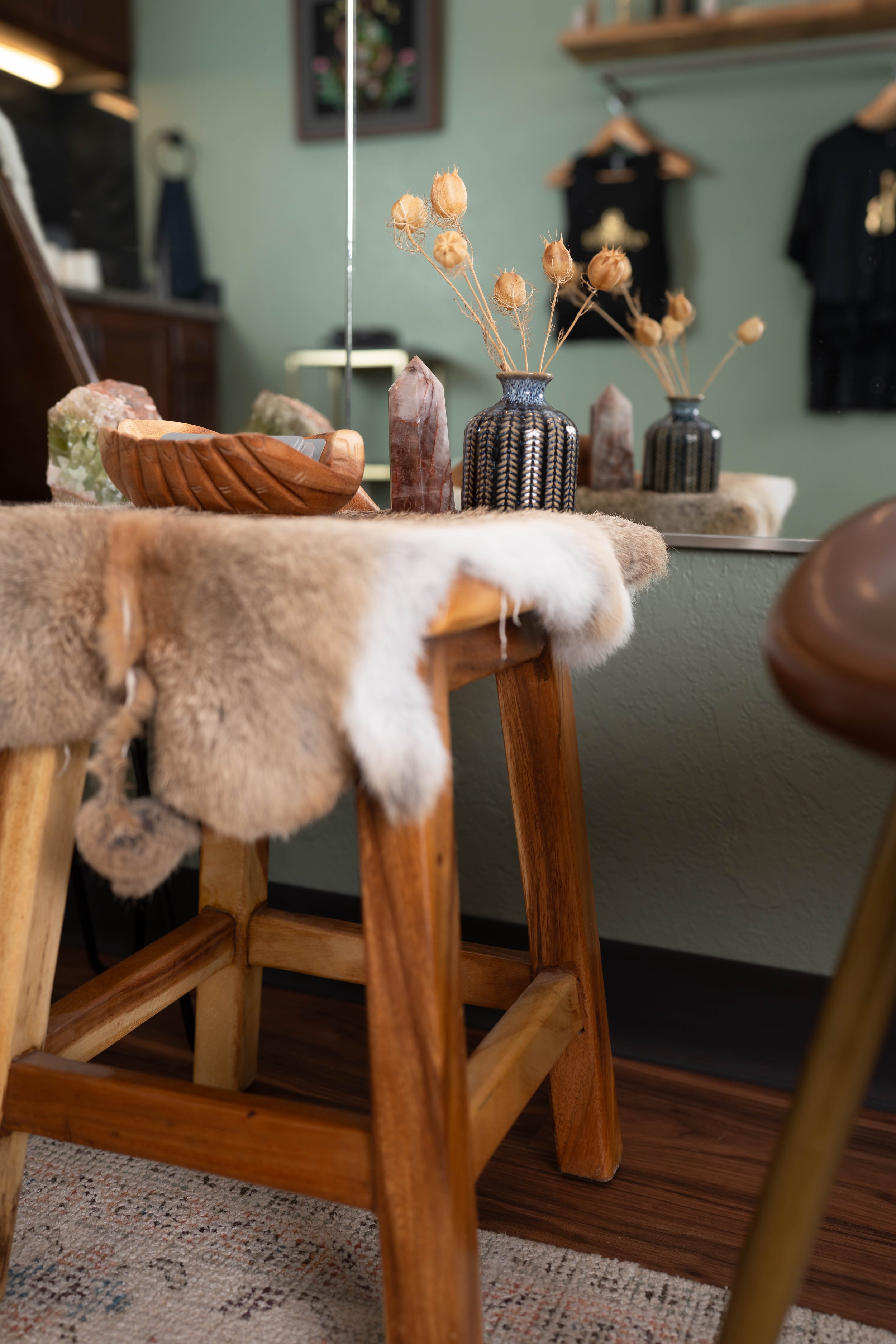 Decorative table with vases, dried flowers, and crystals, with a fur-covered wooden chair in a cozy room.