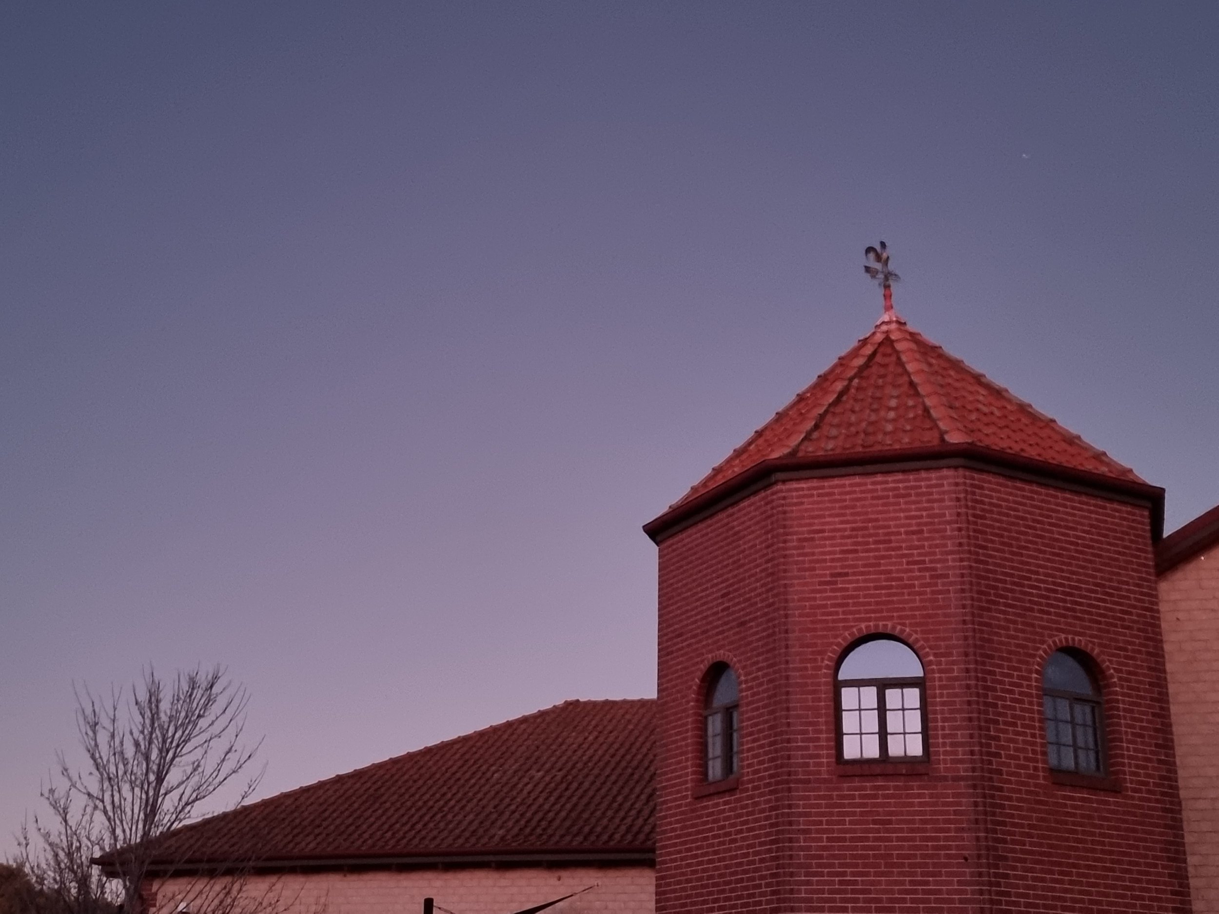 Red brick building with a turret topped by a weather vane against a twilight sky