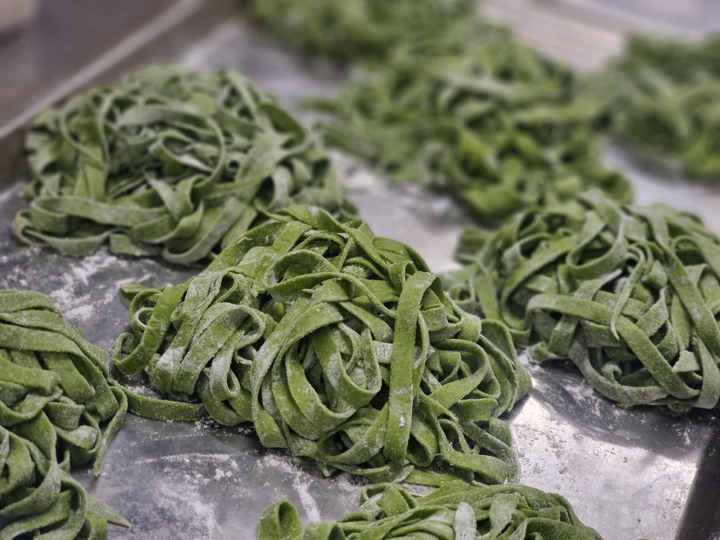 Fresh green spinach fettuccine pasta nests dusted with flour on a baking sheet