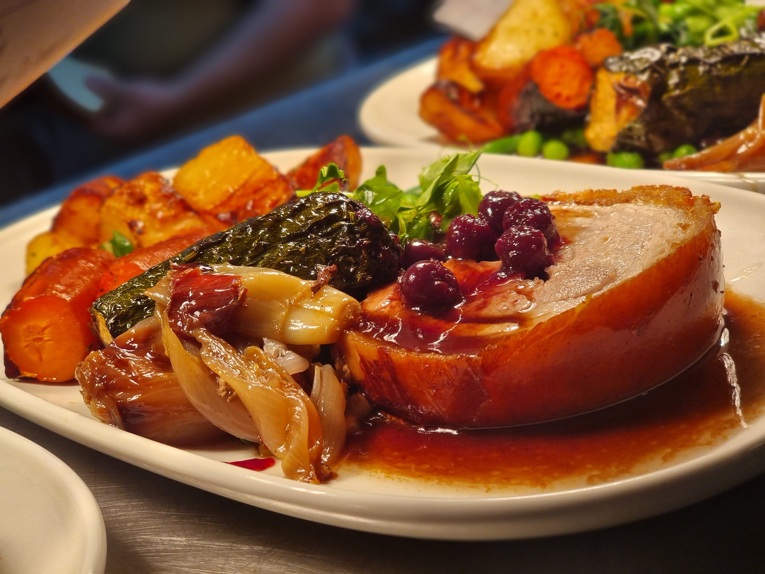 Roast pork served with gravy, roasted vegetables, and greens on a white plate.