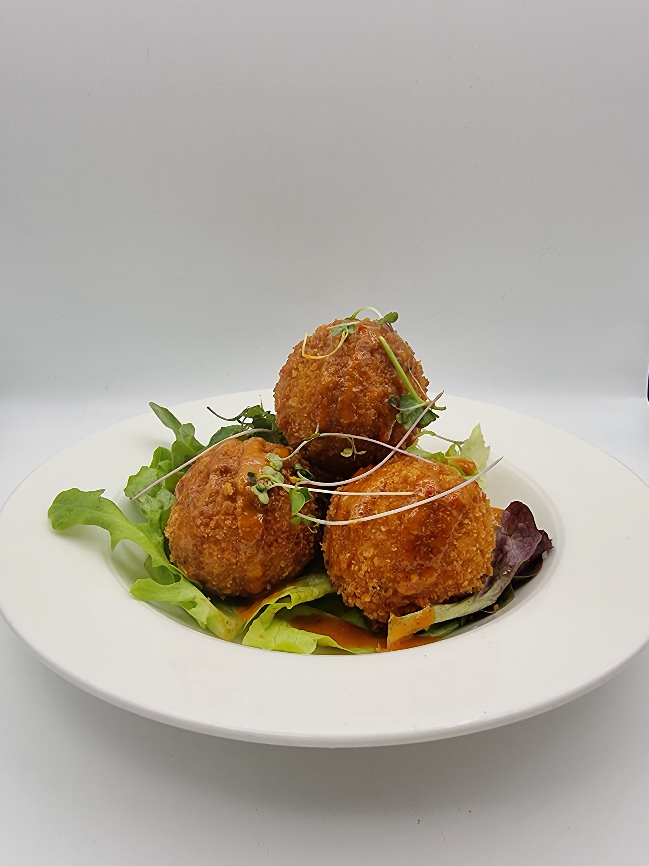 Three fried croquettes garnished with microgreens served on a bed of mixed greens in a white bowl.