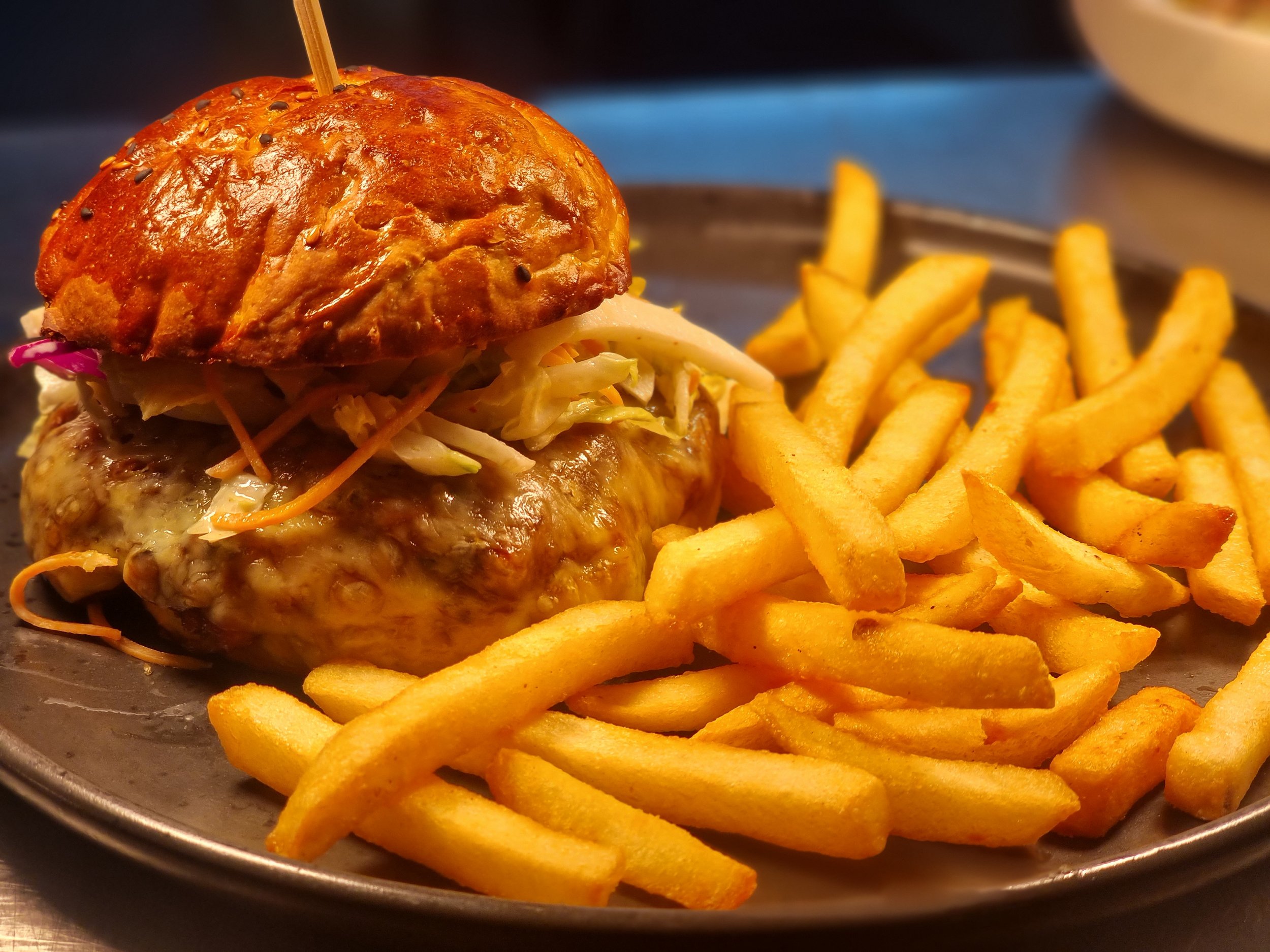 A cheeseburger with a toasted bun, lettuce, and cheese, served with a side of French fries on a dark plate.