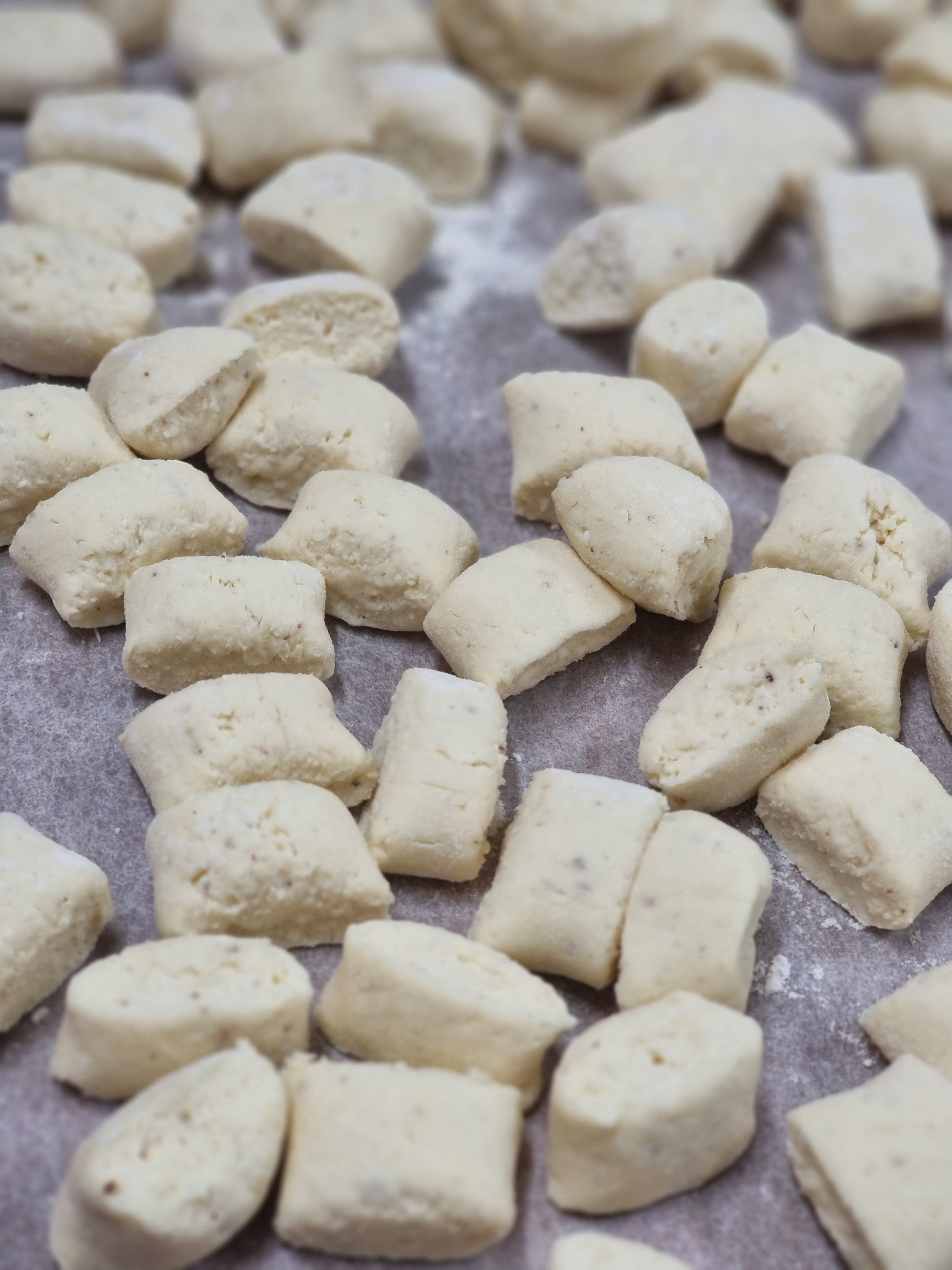 Uncooked gnocchi dough pieces on parchment paper.
