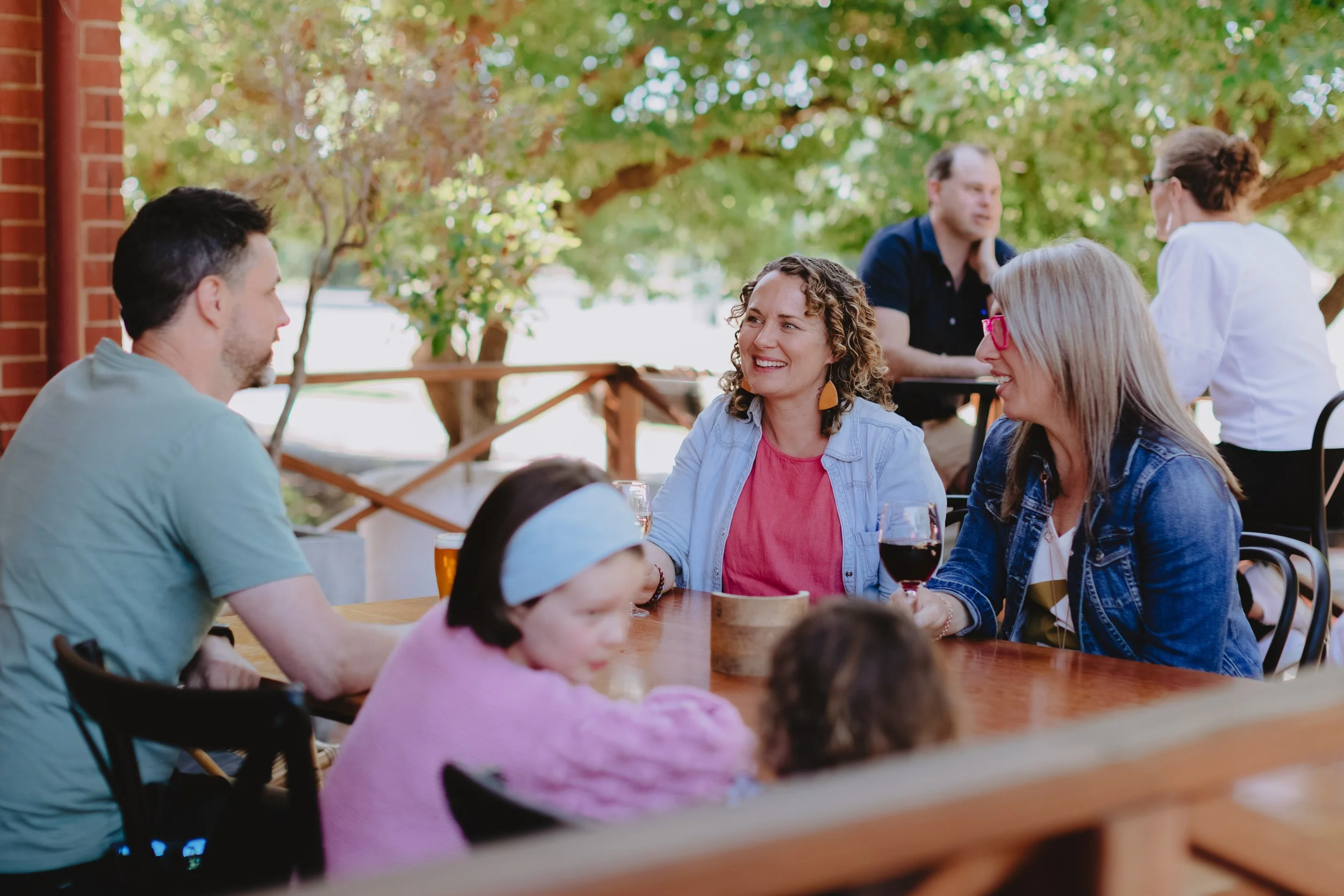 Group of people socializing outdoors at a sunny patio, enjoying drinks and conversation.