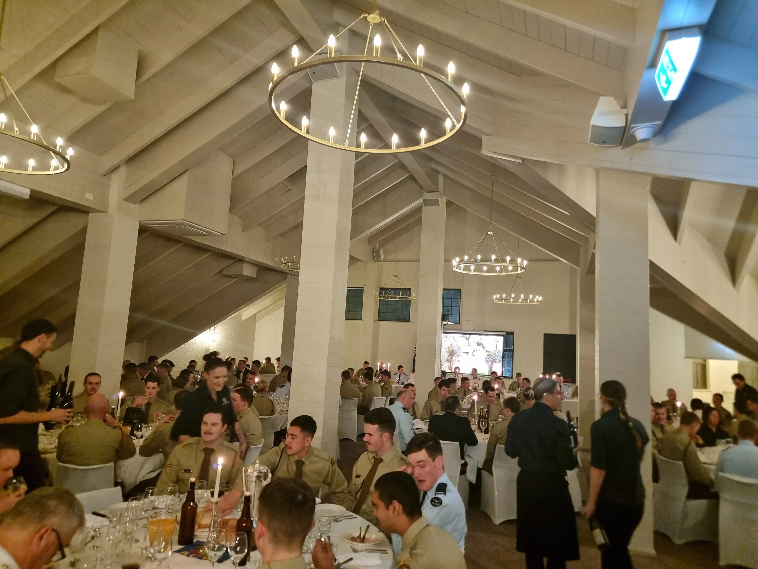 People in military uniforms dining in a decorated banquet hall with circular chandeliers.