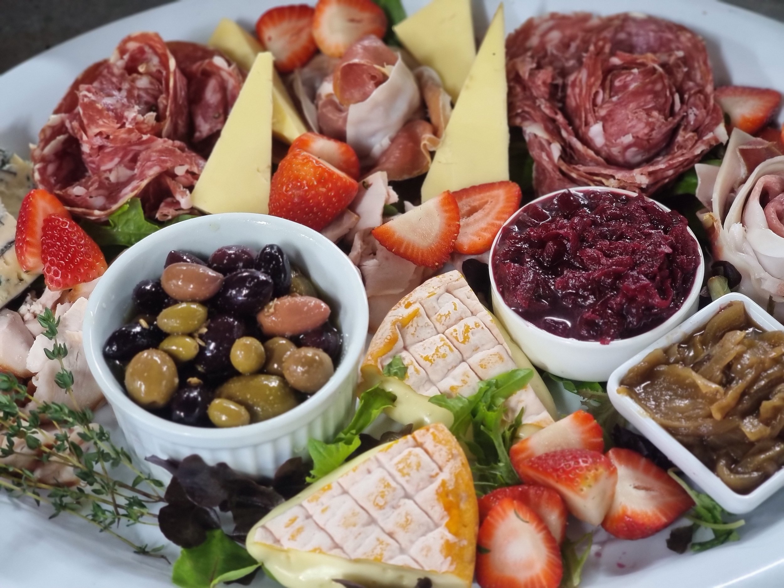 A platter of assorted cheeses, cured meats, strawberries, olives, and fruit preserves.