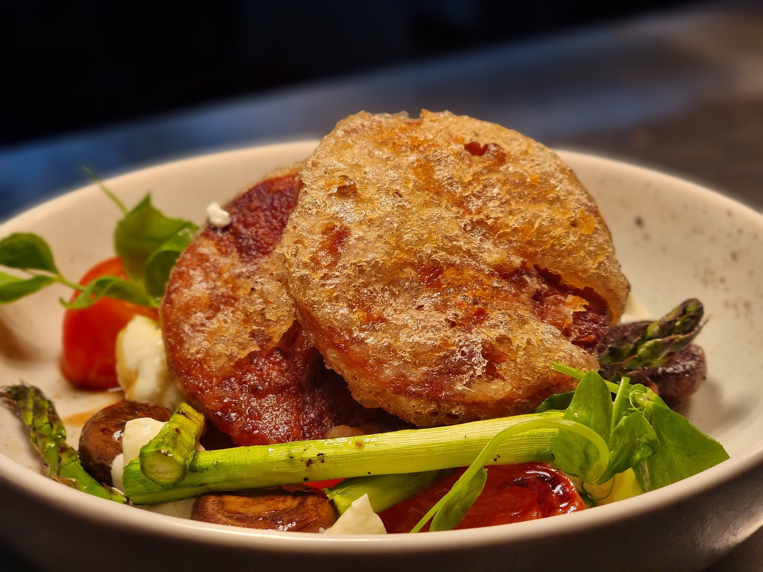 Fried chicken with vegetables in a white bowl, including asparagus, cherry tomatoes, and greens.