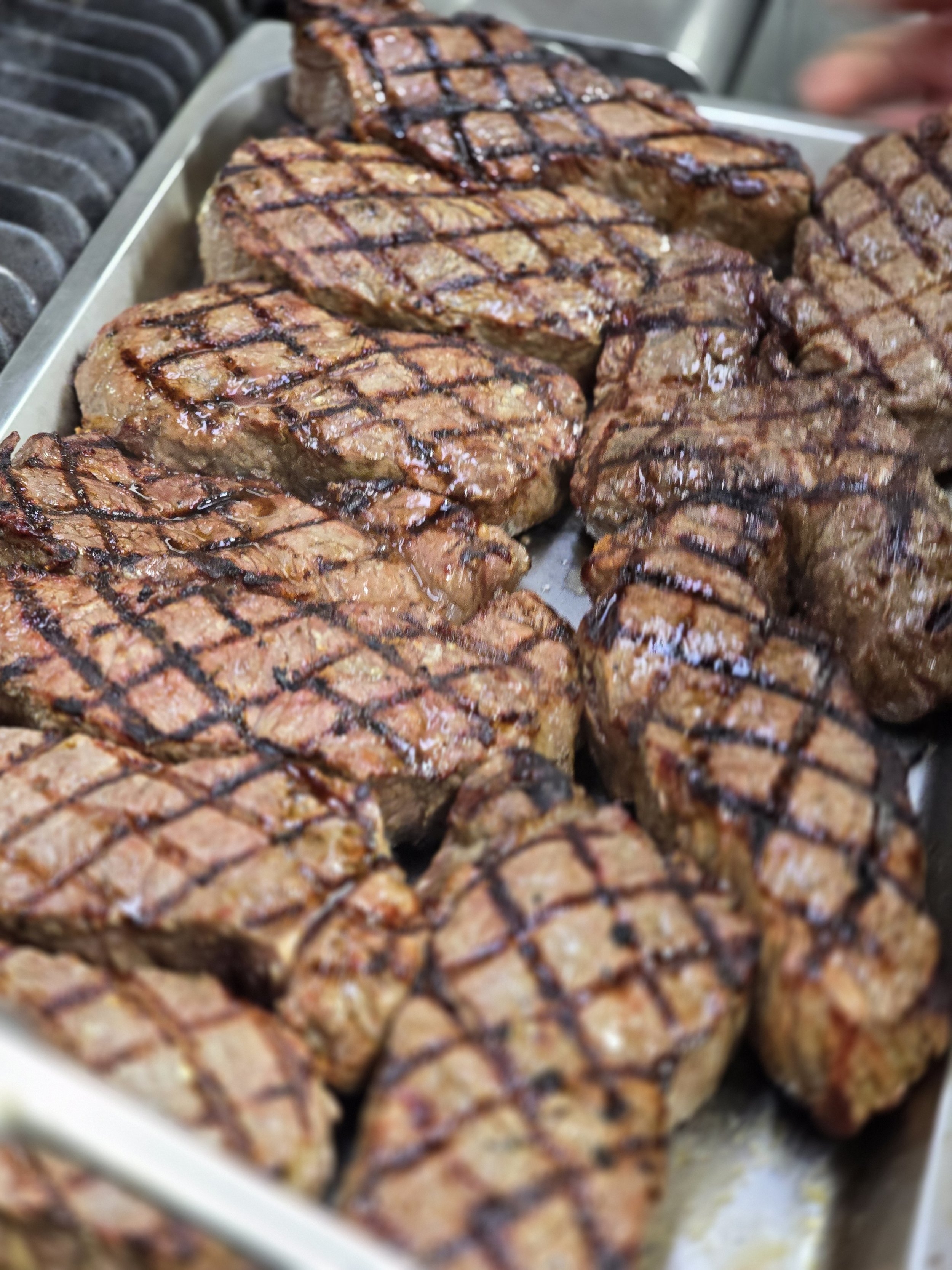 Grilled steaks with crosshatch grill marks on a metal tray.