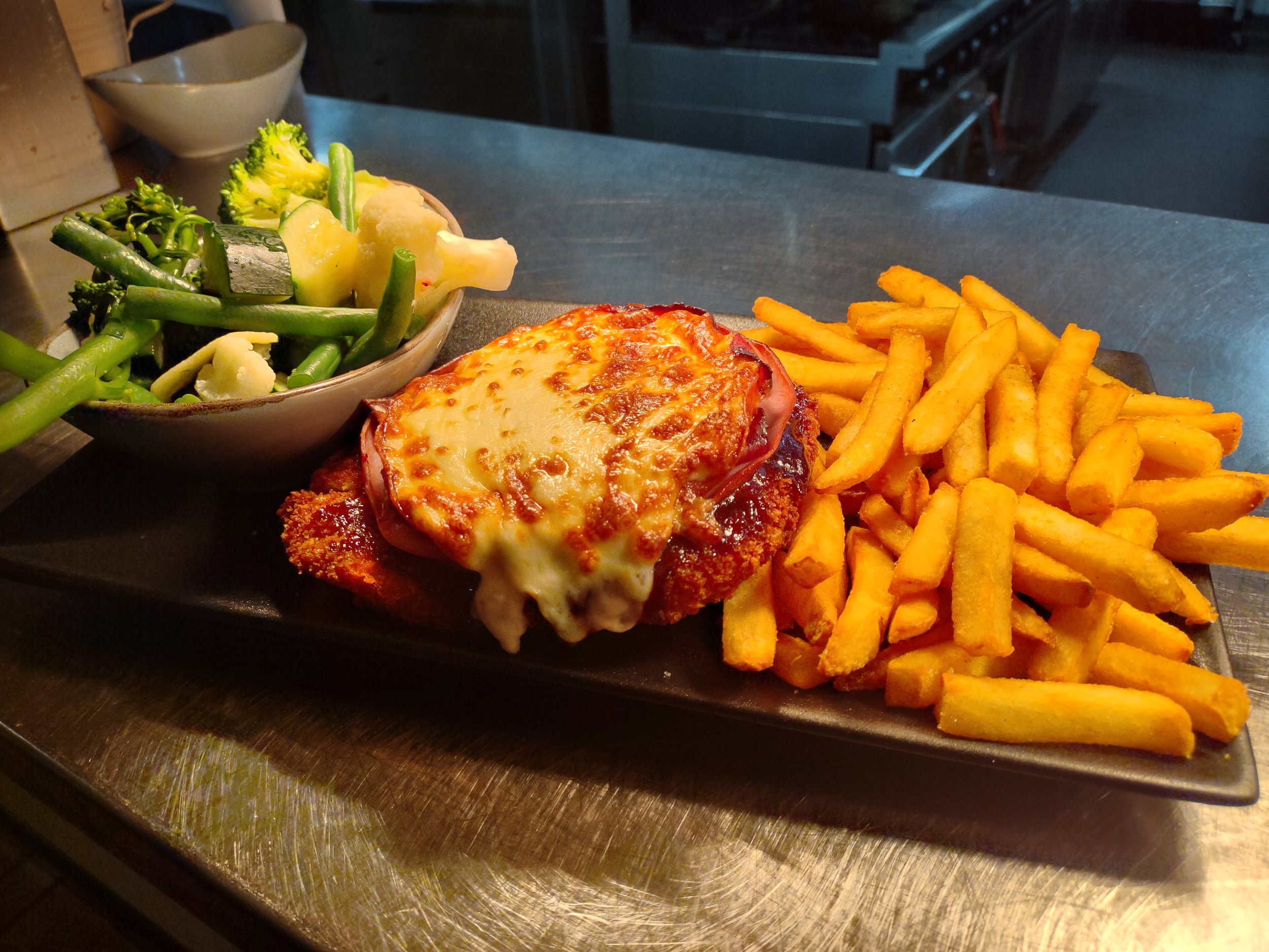 Plate with French fries, a breaded chicken topped with melted cheese and pepperoni, and a side of mixed vegetables including broccoli and green beans.