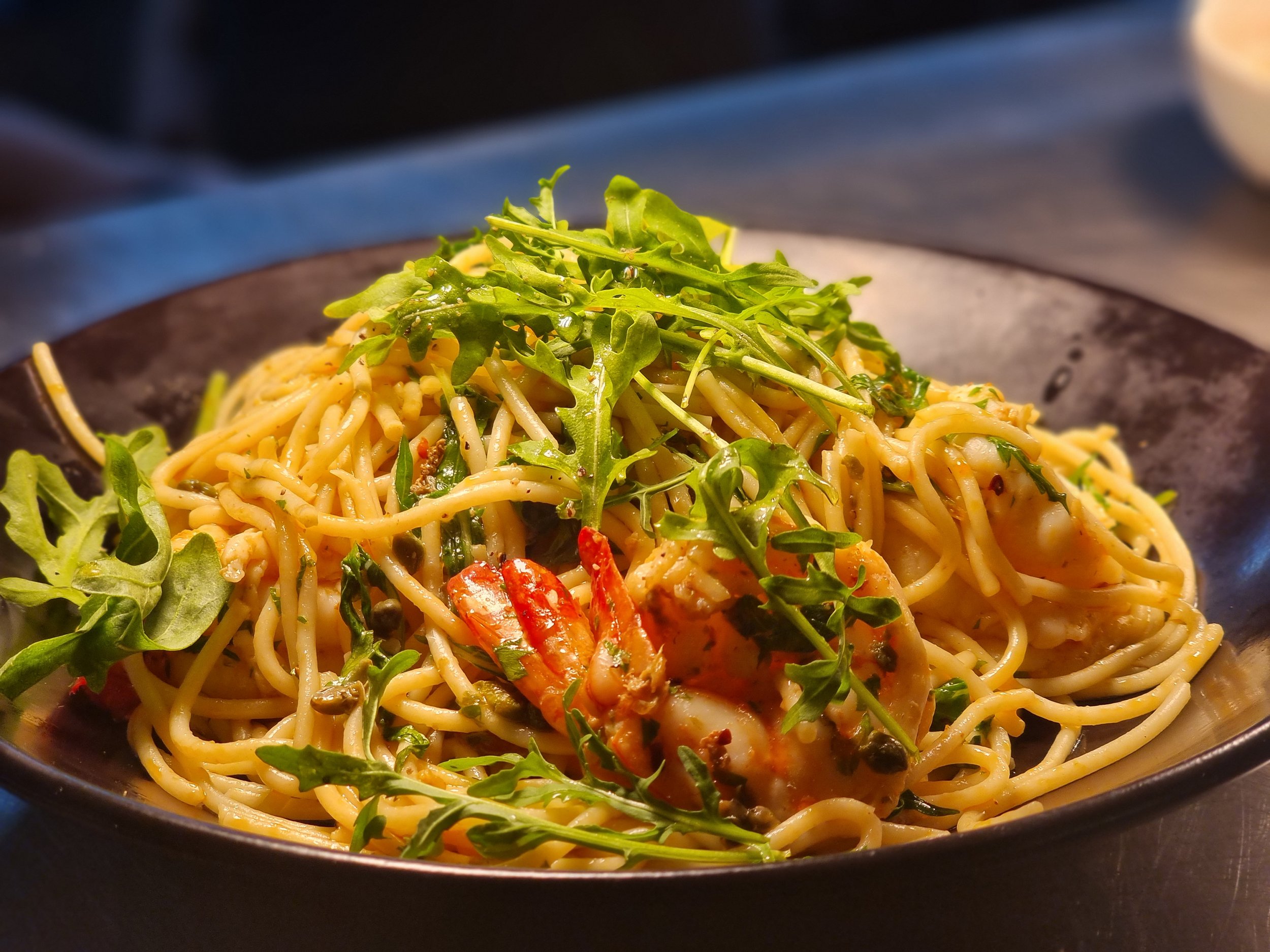 A plate of cooked spaghetti pasta with leafy greens and shrimp, garnished with fresh herbs.