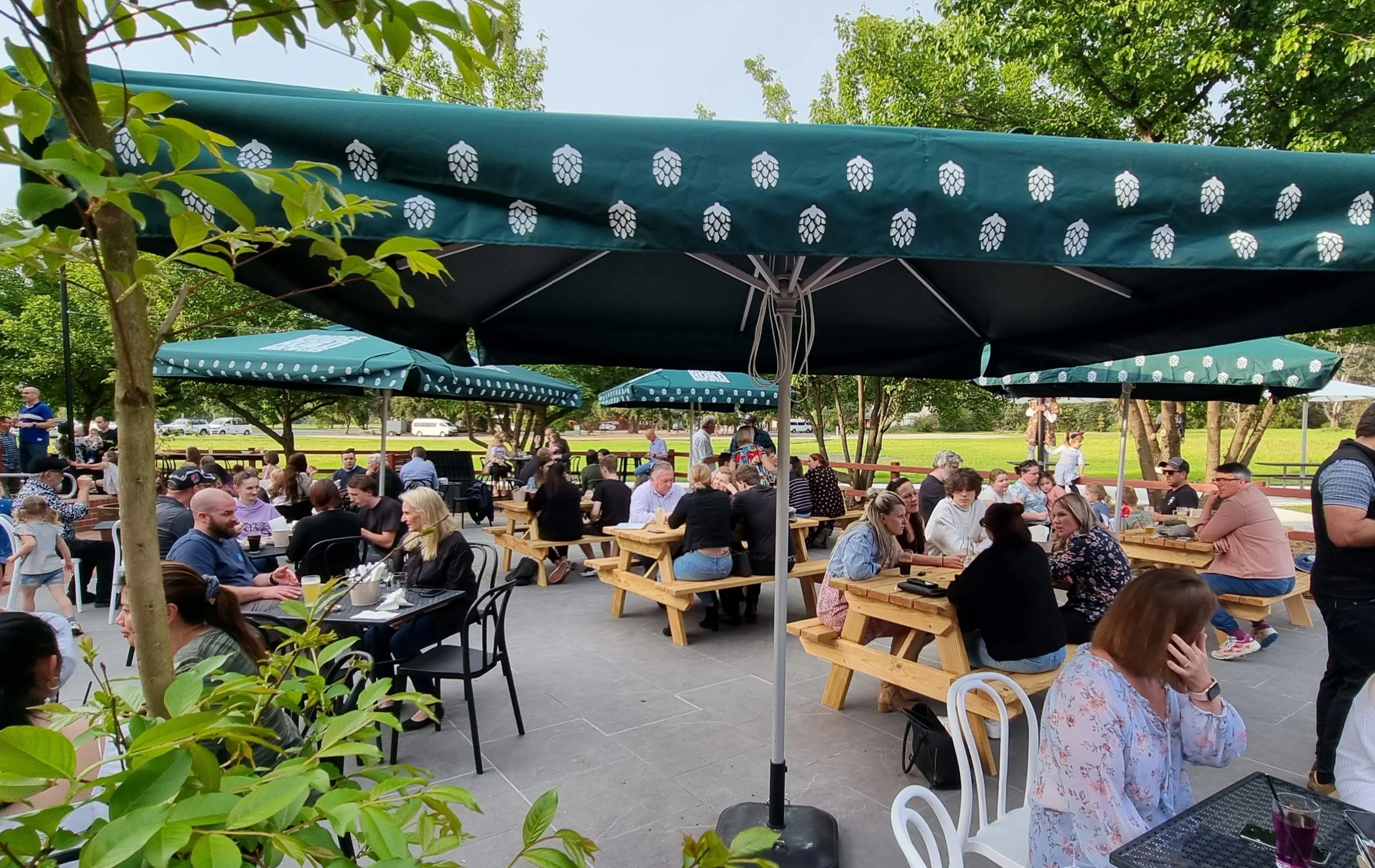 People enjoying outdoor dining at a patio with umbrellas and trees in the background.