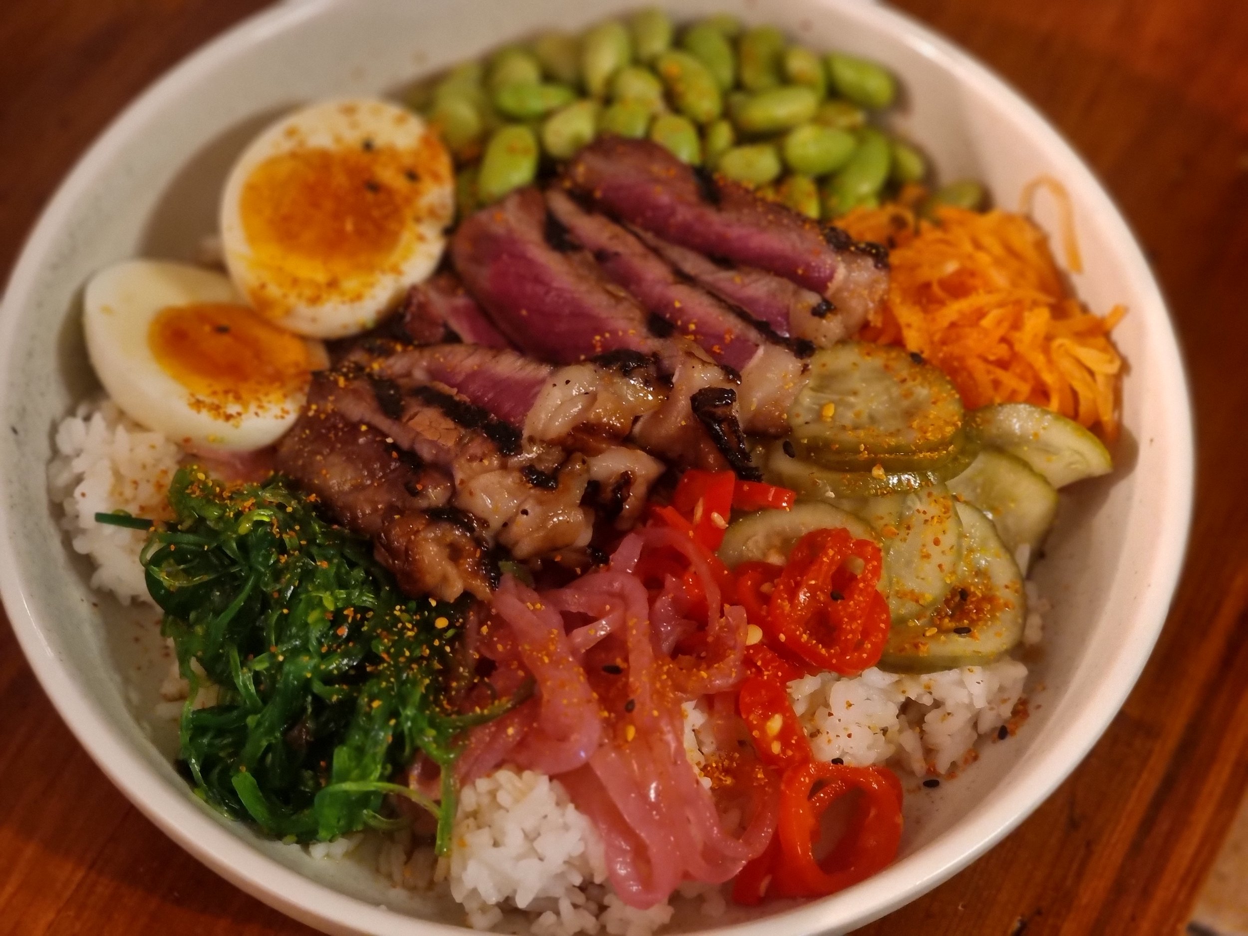 Bowl of Korean bibimbap with rice, sliced beef, boiled eggs, spinach, kimchi, cucumber, peppers, and assorted vegetables.