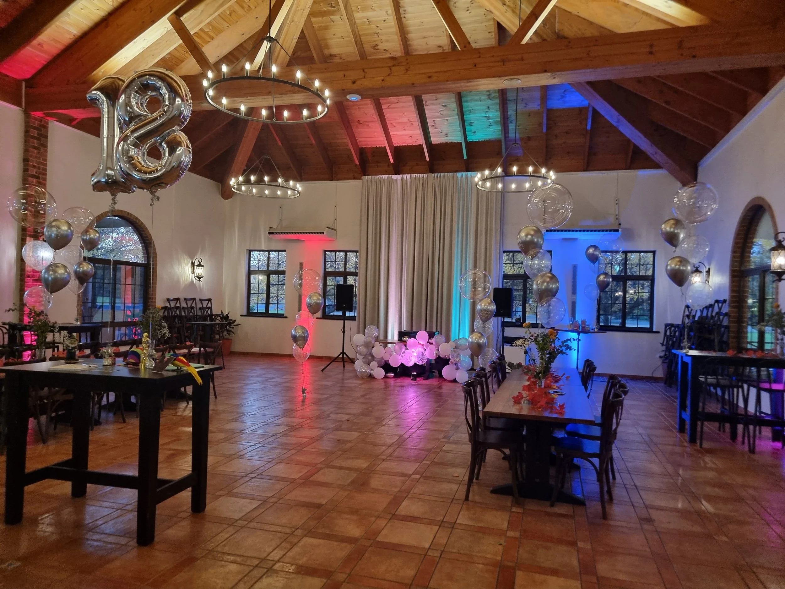Decorated event space celebrating 28th birthday, with balloons, tables, and colorful lighting in a rustic wooden hall.